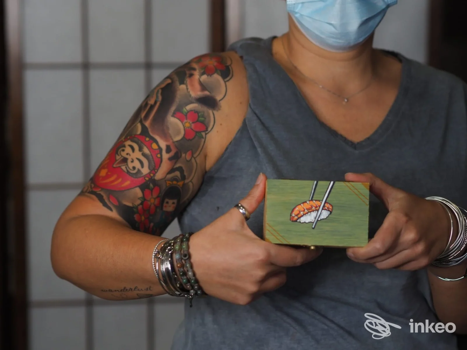 Dettaglio di tatuaggio colorato sul braccio superiore di una cliente in Only Ink Tattoo Studio, San Donà di Piave; persona con mascherina tiene un piccolo oggetto.