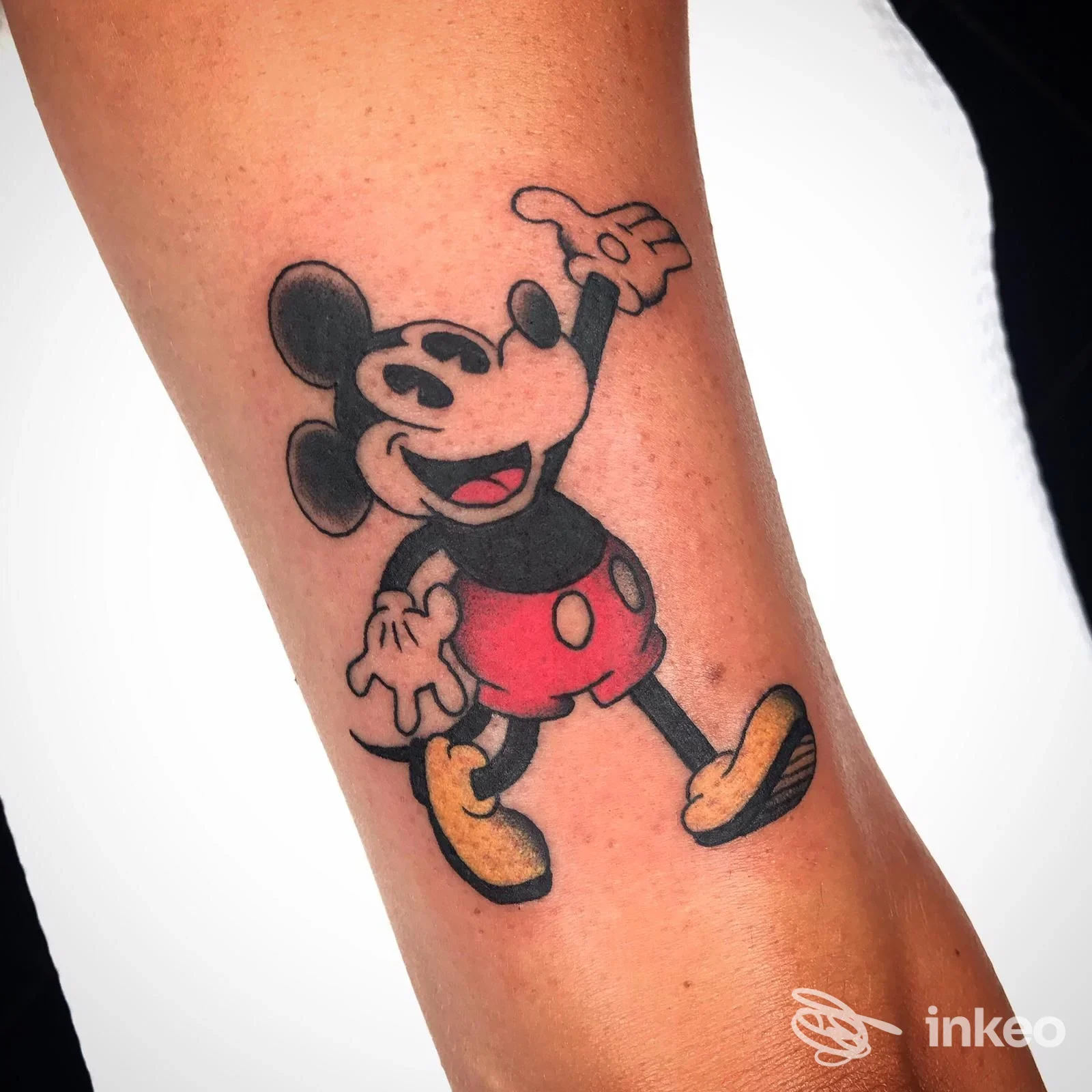 Tatuaggio in stile cartoon di Mickey Mouse sull'avambraccio, realizzato da Ink Hustler a Genova con linee nette e colori pieni.