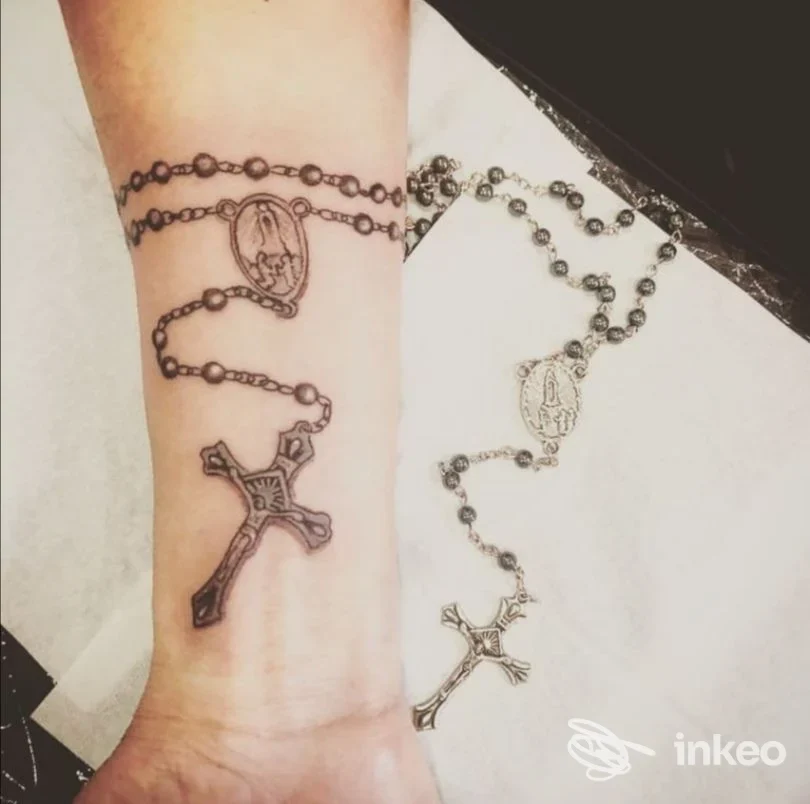 Primo piano del polso e avambraccio con tatuaggio a forma di rosario affiancato al rosario metallico fotografato sul tavolo, Tattoo & Dreams, Prato.