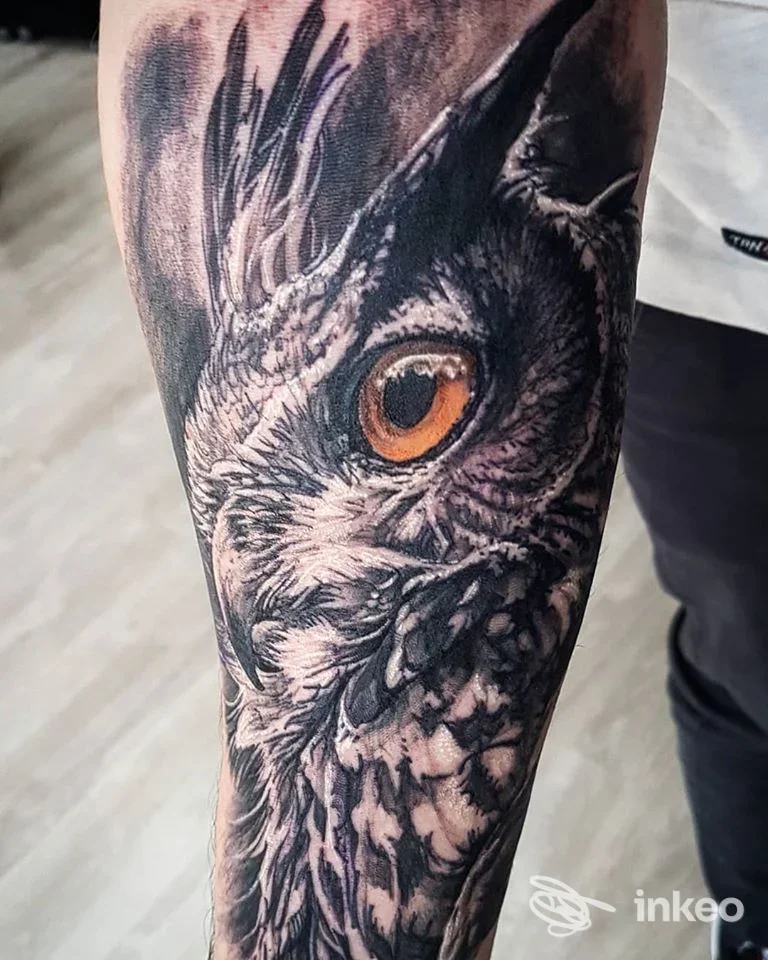 Dettaglio di tatuaggio a tema gufo sull'avambraccio, realizzato da RAM TATTOO a Tivoli, stile realistico con toni neri e occhio arancione.