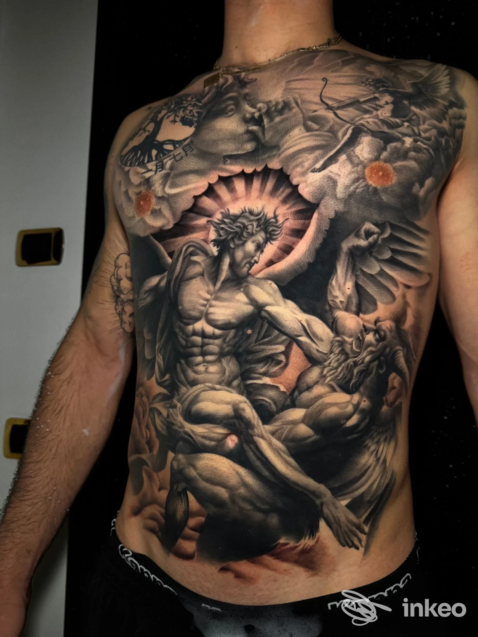 Ampio tatuaggio a tema sacro che copre torace e addome su corpo reale, fotografato in primo piano. Gold Ink - Tattoo & Piercing, Bari.