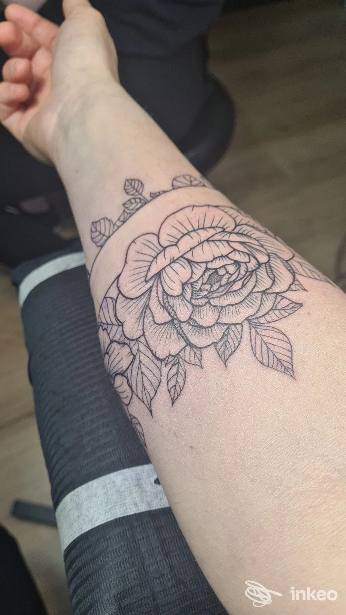 Primo piano di un tatuaggio a linee nere di un grande fiore sull'avambraccio, foto fornita da Baku Tattoo Roma, Roma.