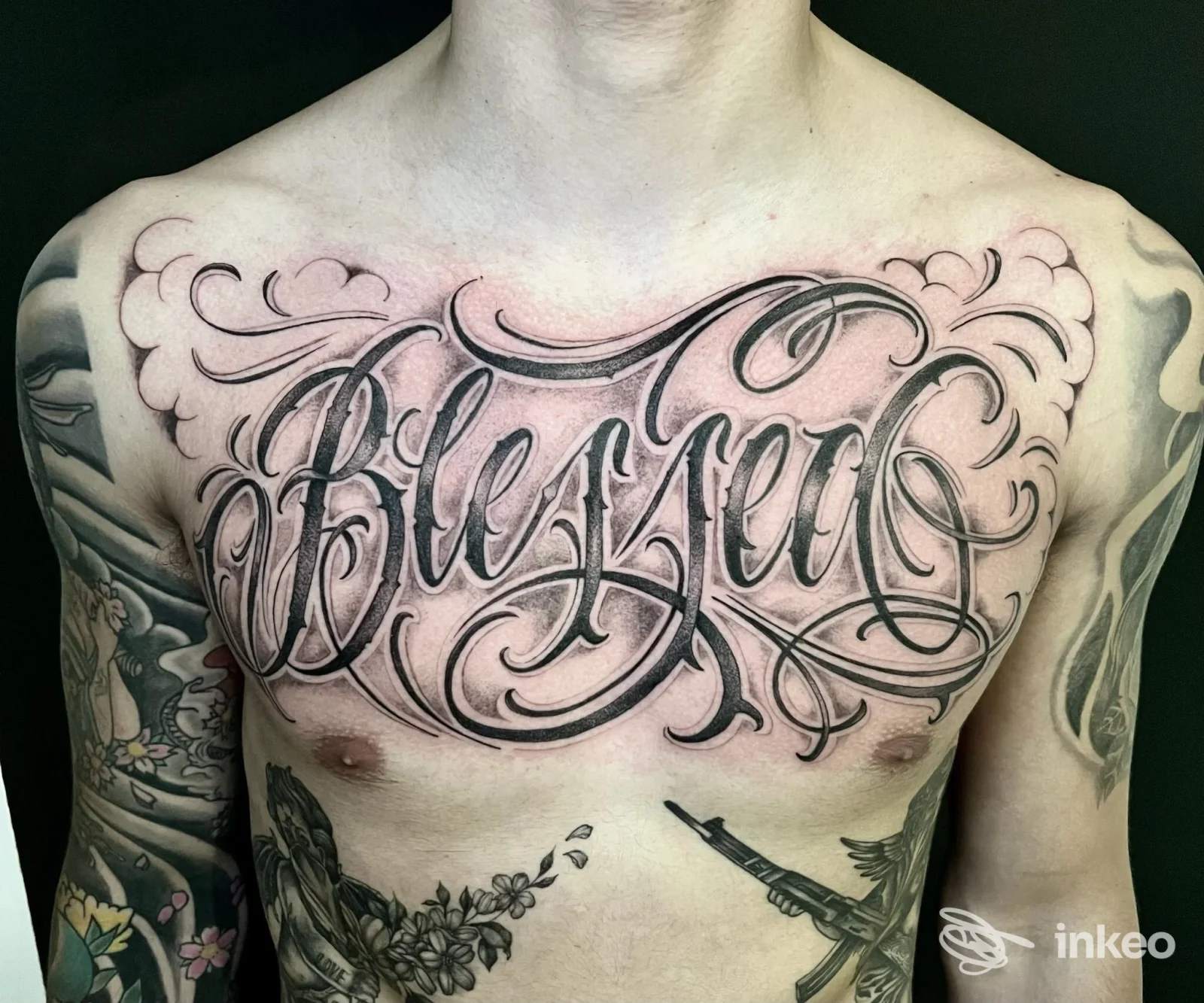 Grande tatuaggio calligrafico 'Blessed' sul petto, realizzato da Paradox Ink a Viareggio, con altri tatuaggi su avambracci e addome.