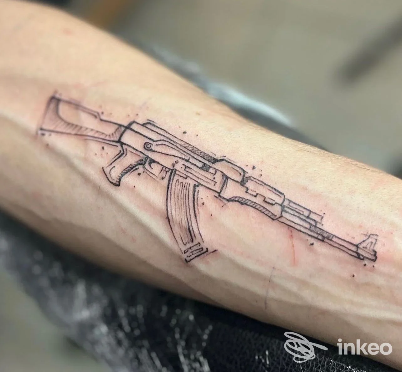 Tatuaggio a linee di un fucile AK-47 sull'avambraccio, lavoro di Psilocybink a Taggia.