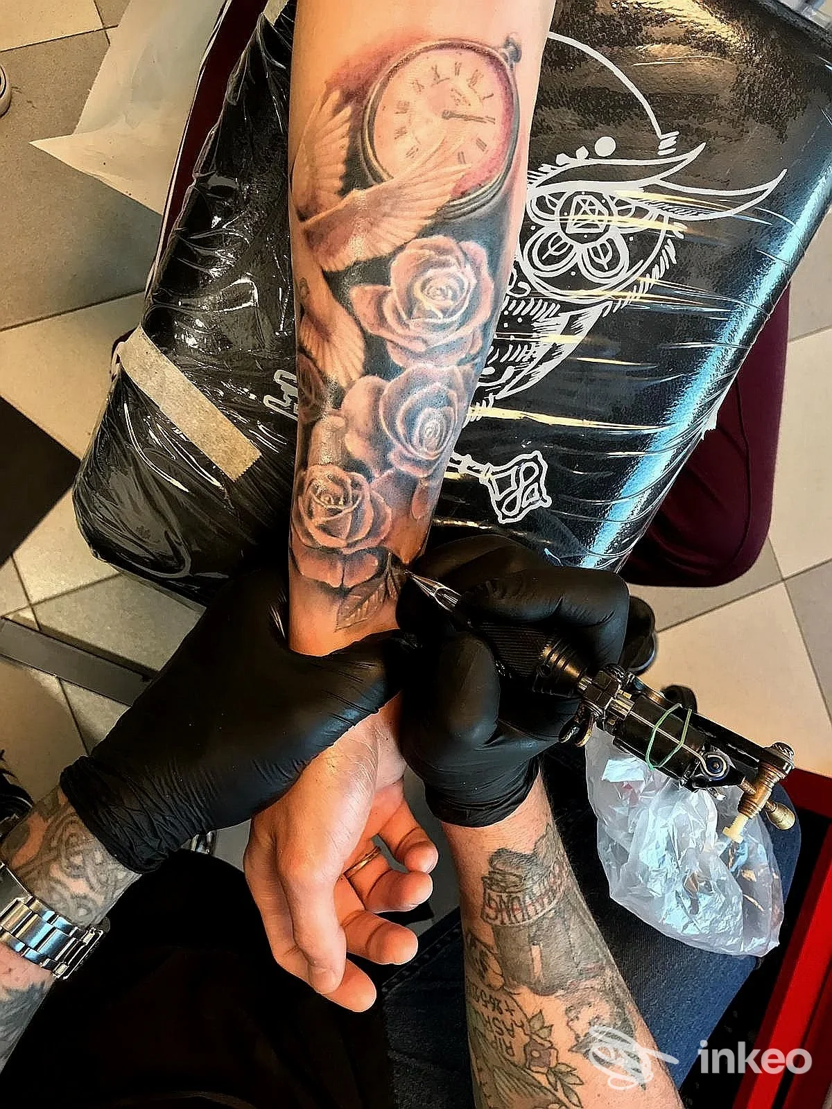 Avambraccio tatuato durante una sessione al Pagan Tattoo Art Studio Ditta G. Maccotta, Latina: orologio, ali e rose in corso di inchiostrazione.