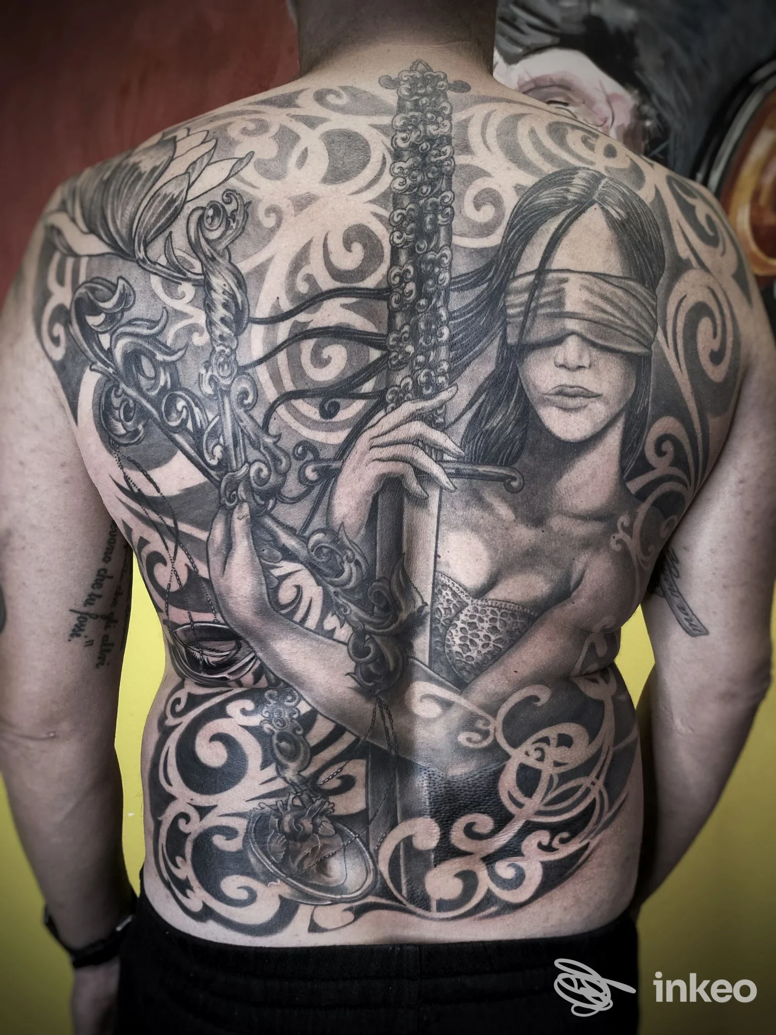 Ampio tatuaggio in bianco e nero sulla schiena con figura bendata e spada, foto fornita da Planet052, Treviso.