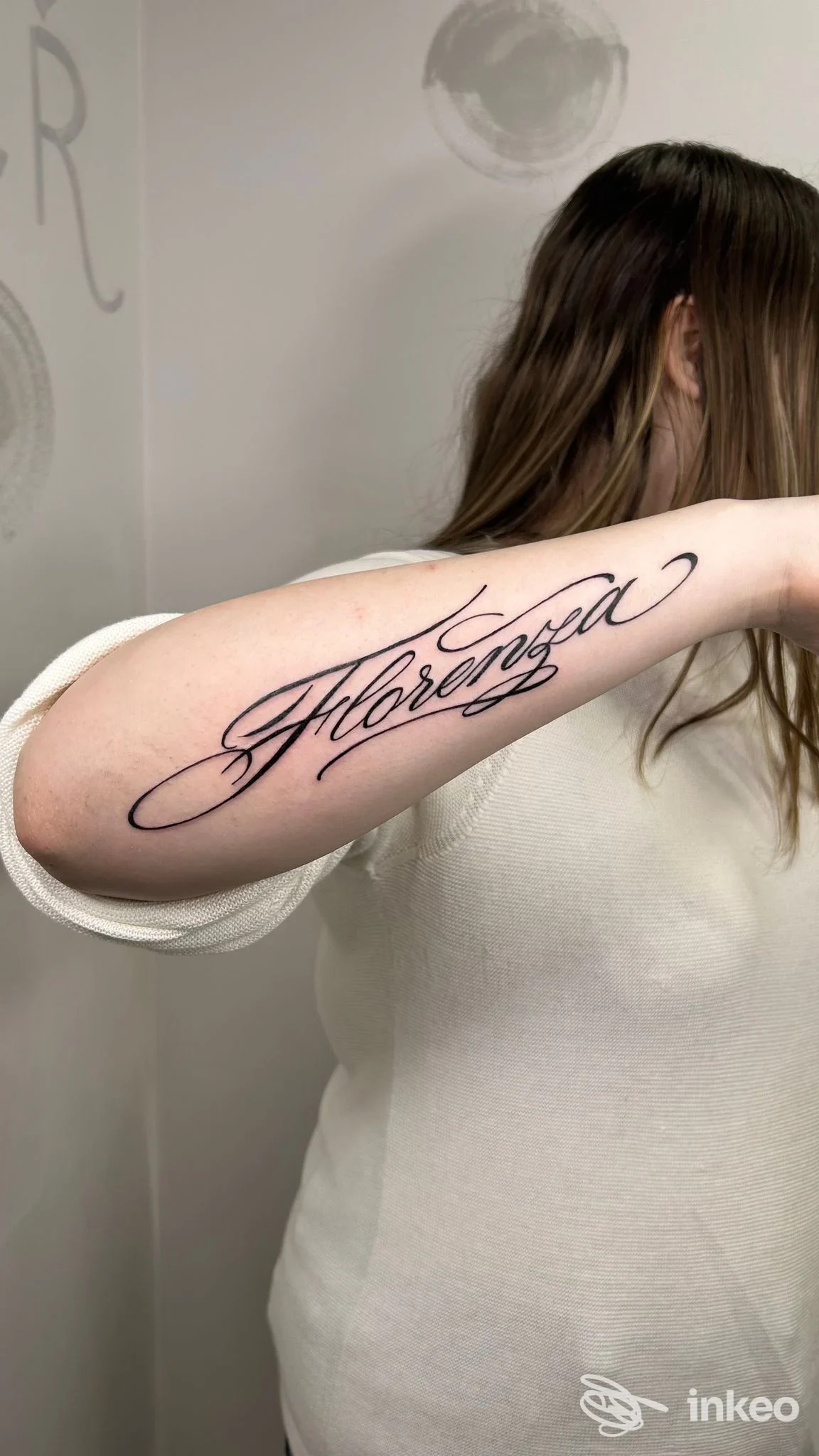 Tatuaggio scriptato visibile sull'avambraccio di una persona in studio, senza volto visibile.