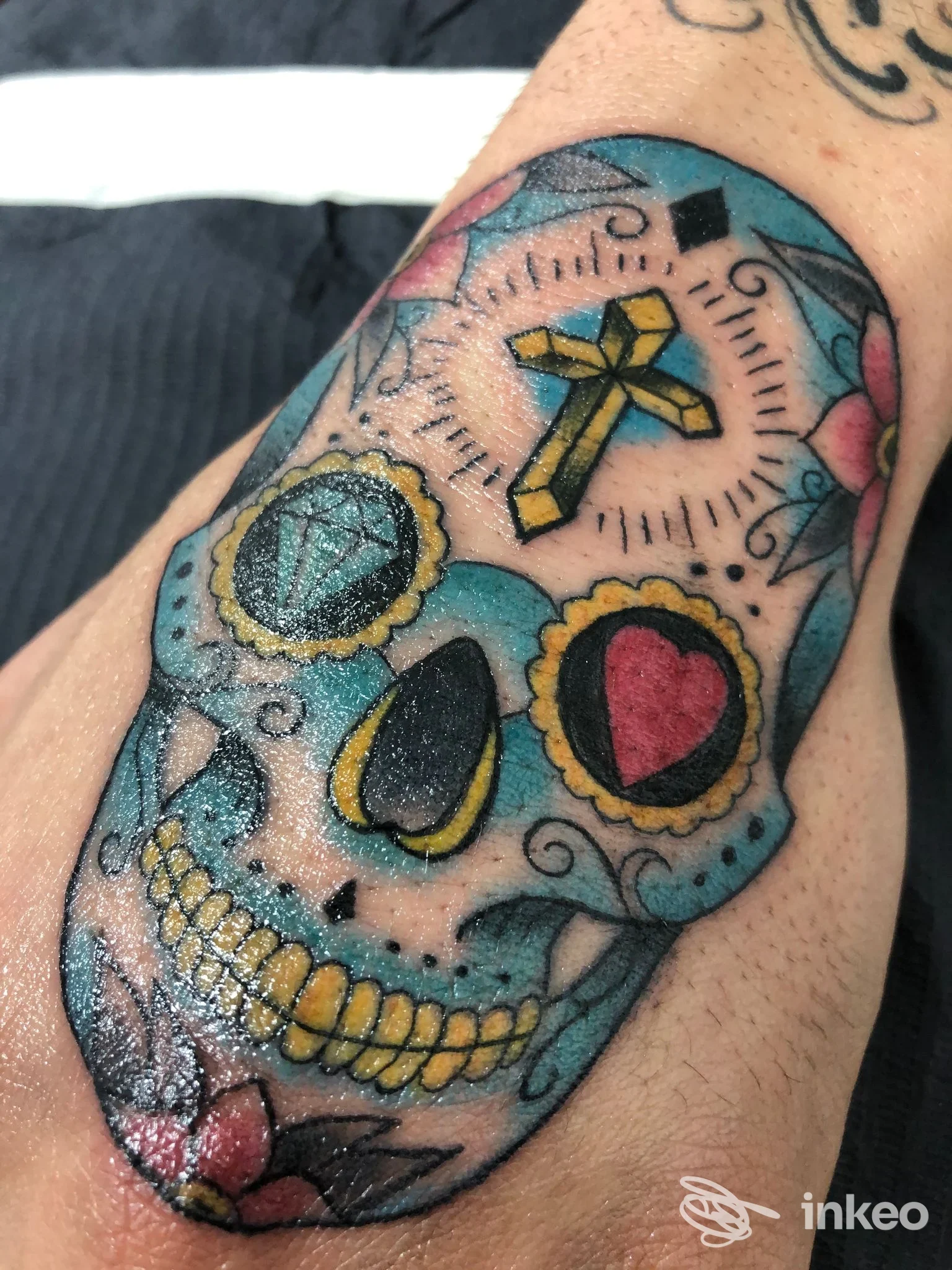 Tatuaggio colorato a tema teschio con croce e gemme, realizzato da Inked Up Tattoo Shop a Sabaudia sul dorso della mano.