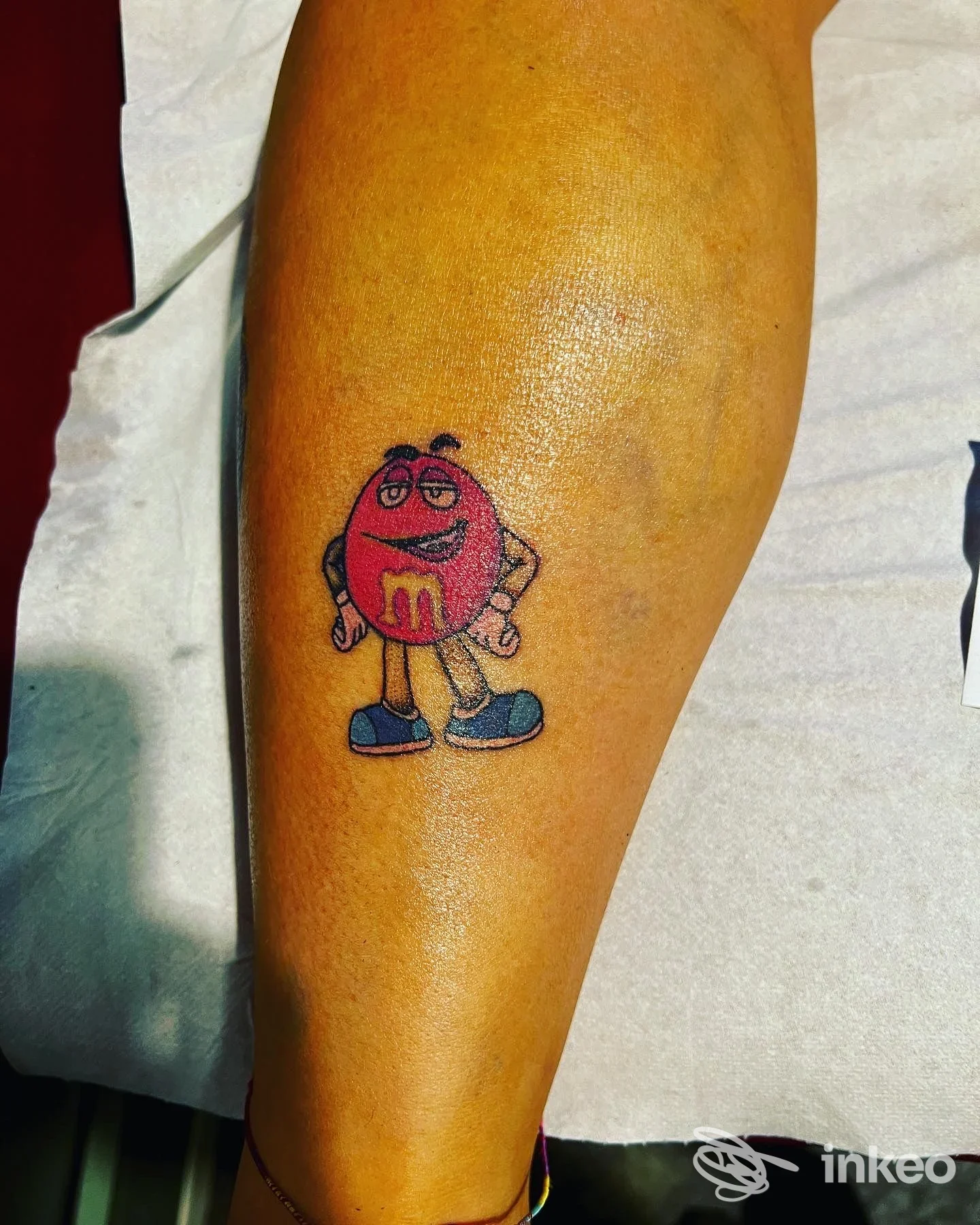 Tatuaggio colorato sul polpaccio raffigurante il personaggio M&M rosso, scattato presso Curu tattoo a Casazza.