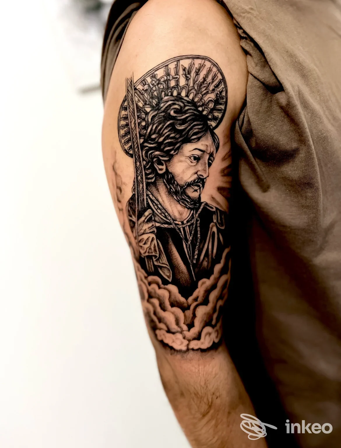 Tatuaggio ritratto black & grey sul braccio superiore, scatto che mostra i dettagli dell'aureola e delle nuvole. INTOSTREET - ink & beauty, Montescaglioso.