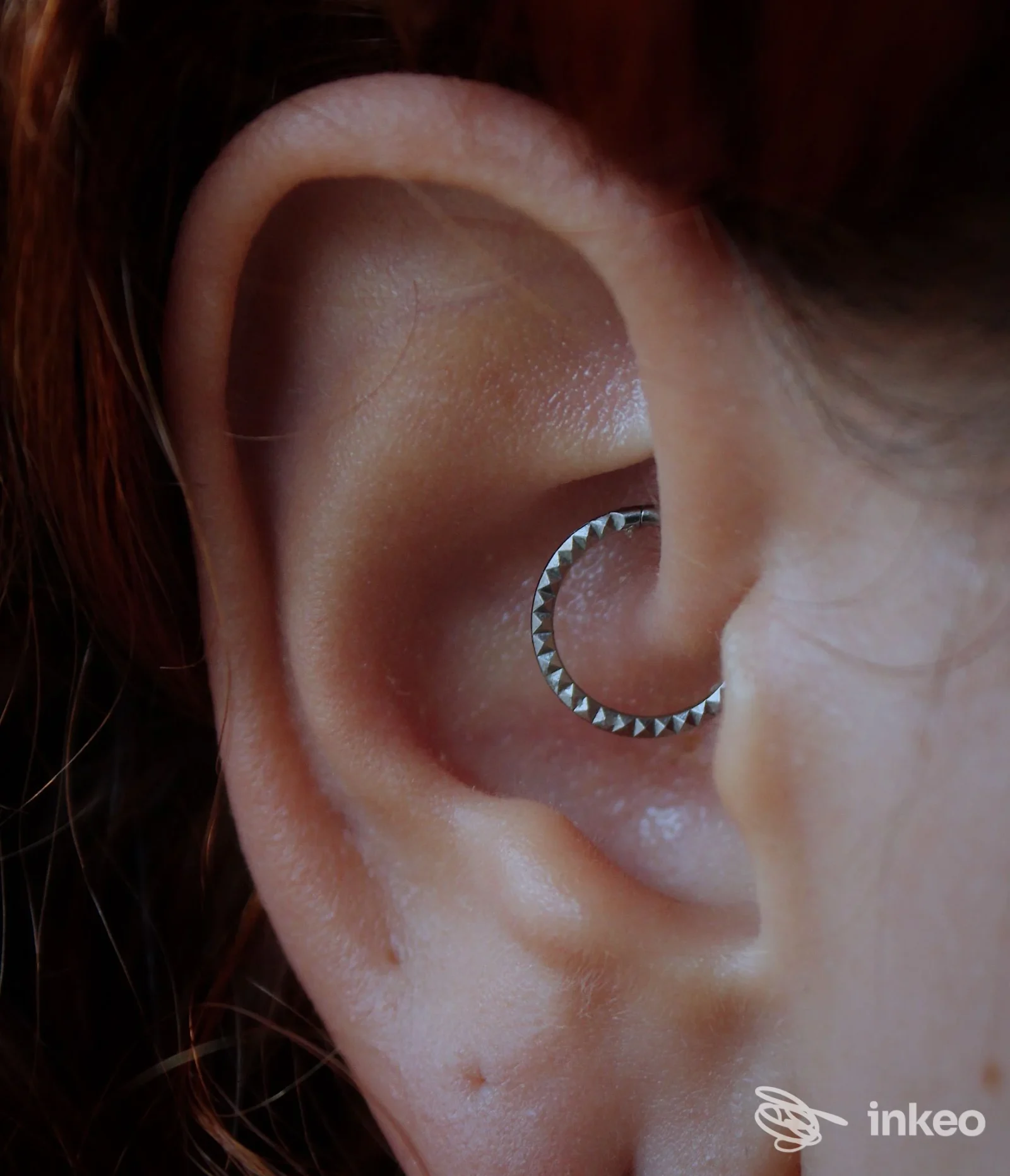 Orecchio di una persona con piercing circolare in cartilagine, anello metallico con piccole punte visibile sull’esterno dell’orecchio; nessun volto visibile.