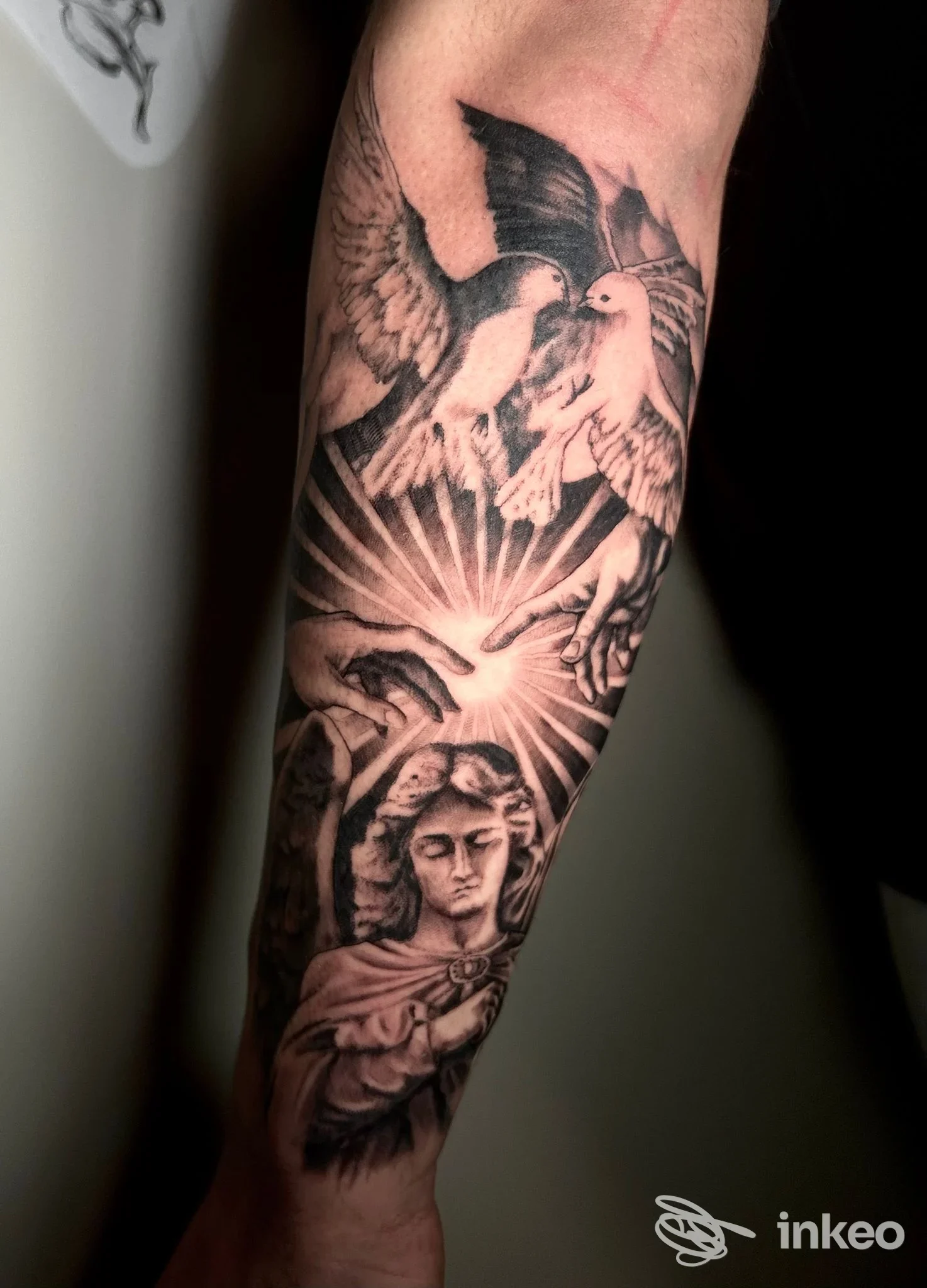Tatuaggio in bianco e nero su avambraccio con colombe, mani che si toccano e figura scultorea, Astro Zombie, Città di Castello.