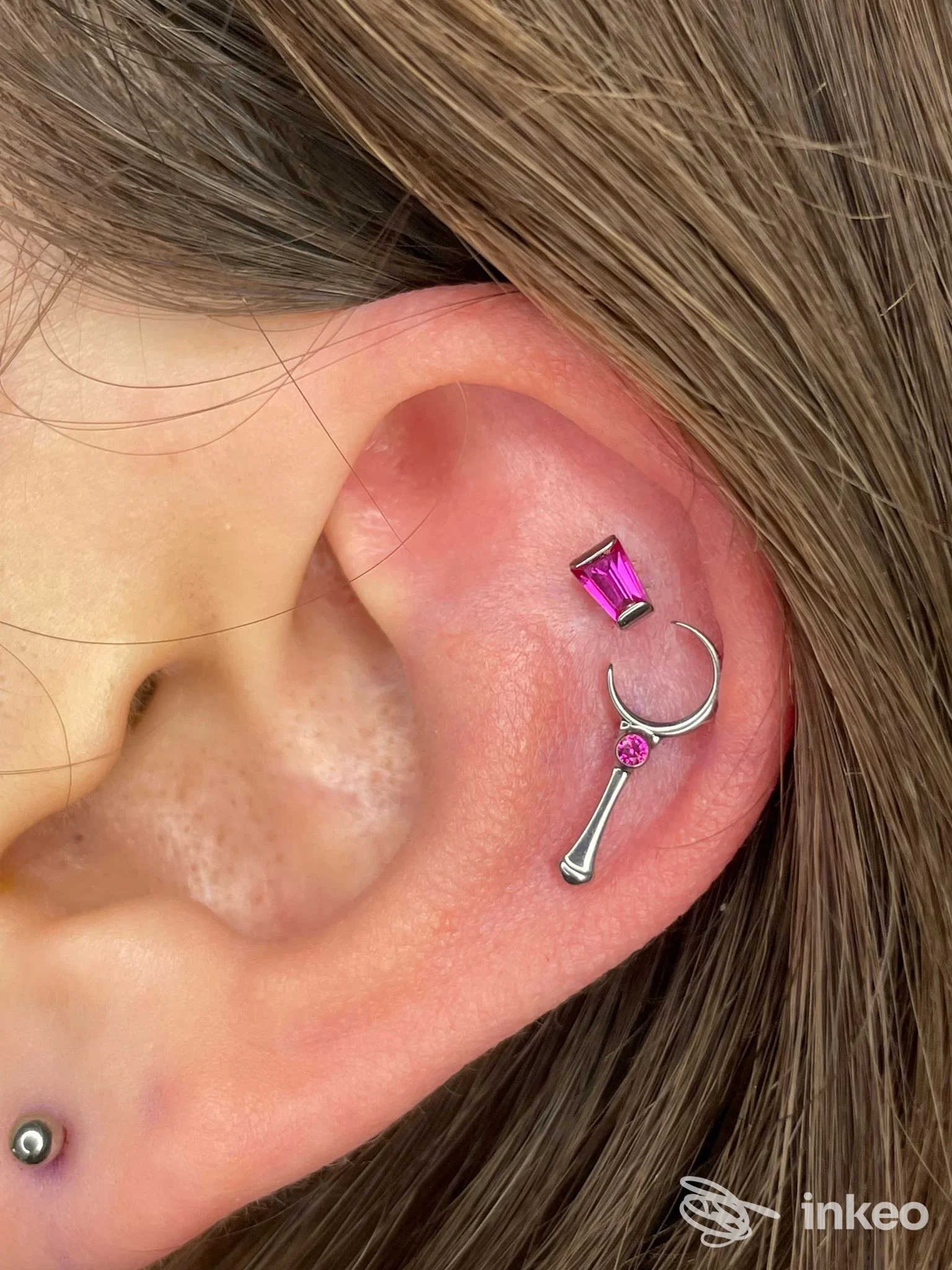 Primo piano di un orecchio con più piercing e gioielli fucsia, scattata per Xenia Body Art a Badia Polesine.