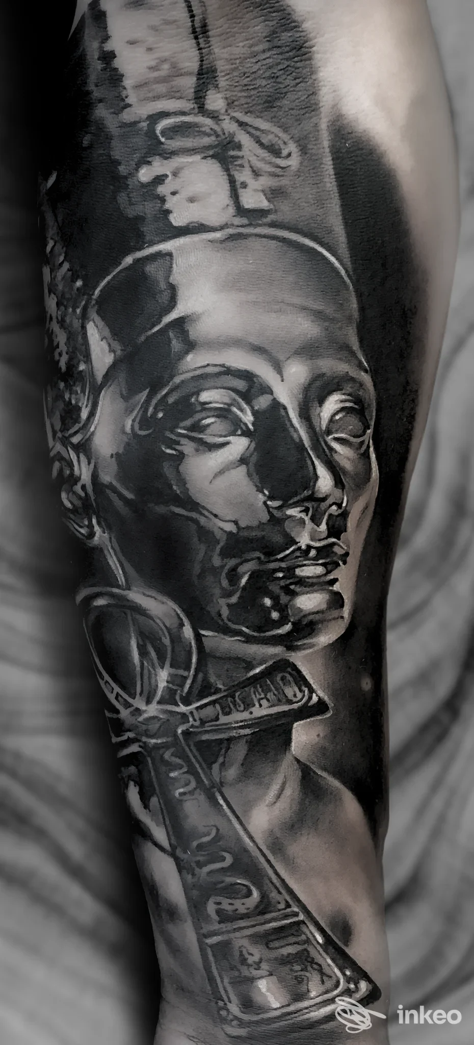 Tatuaggio realistico in bianco e nero su avambraccio con volto stilizzato e ankh — DUENDE, Ceccano.