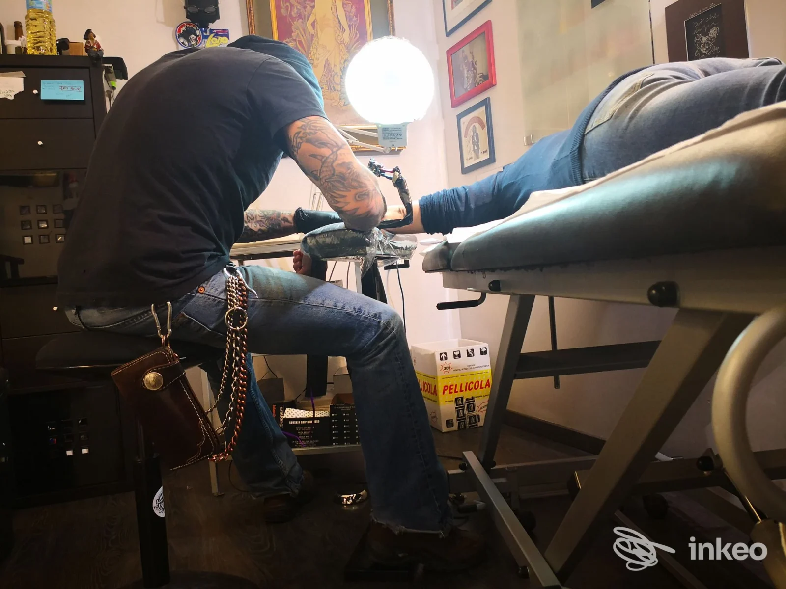 Tatuatore al lavoro nello studio VentoForato Imperia: sessione su avambraccio del cliente con lampada e attrezzatura visibili.