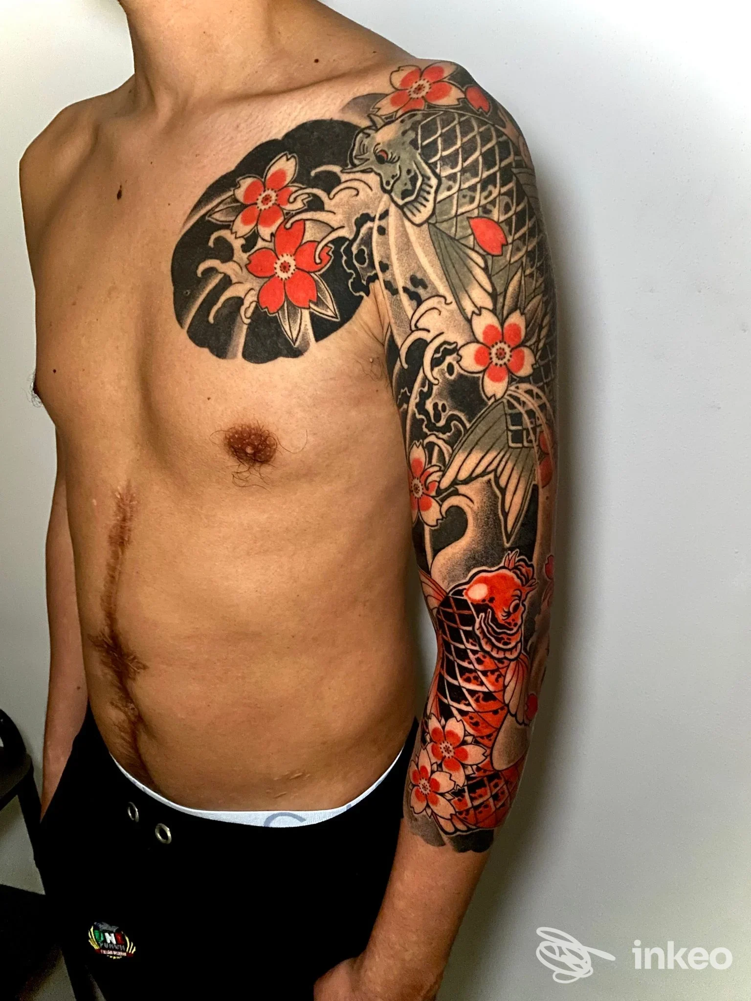 Fotografia di un tatuaggio a manica con carpe e fiori sul braccio destro di un uomo, scattata in studio. Lighthouse Factory, Pisa.