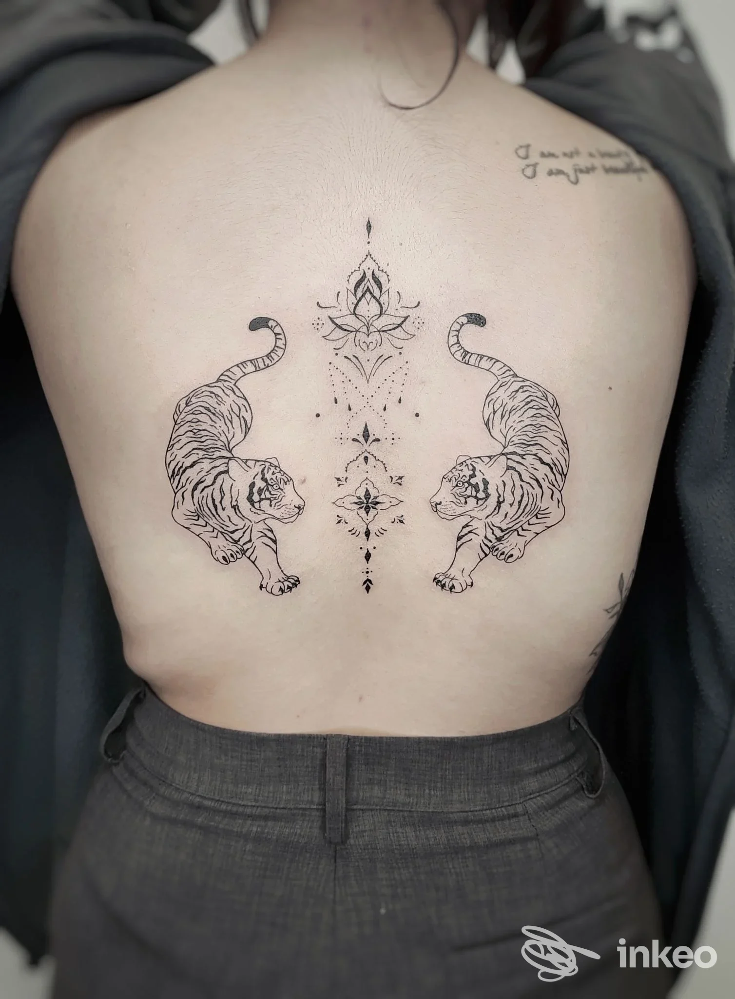 Tatuaggio sulla schiena con due tigri speculari e un decoro ornamentale lungo la linea della colonna vertebrale, lavoro mostrato dallo studio Il Coniglio d'inchiostro a Ponzano Veneto.