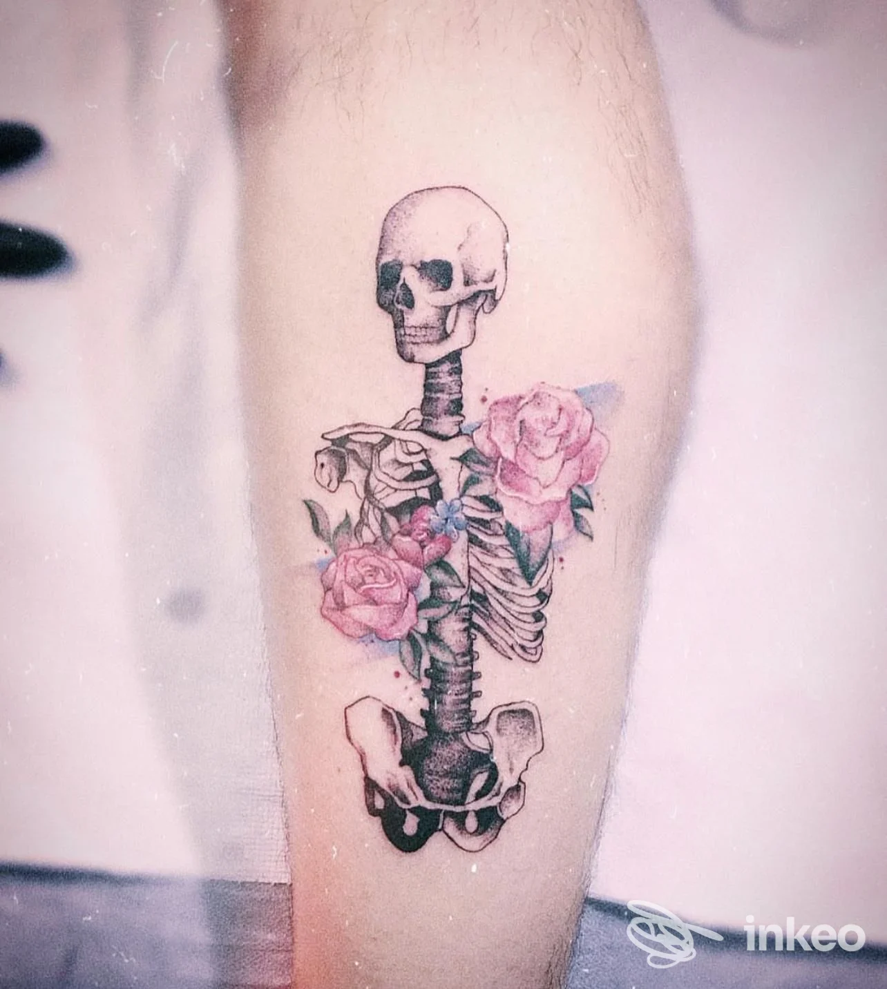 Tatuaggio su pelle raffigurante uno scheletro verticale con rose rosa e foglie, fotografato su arto: lavoro di JAELLOO “la bottega del tatuaggio” a Licata.
