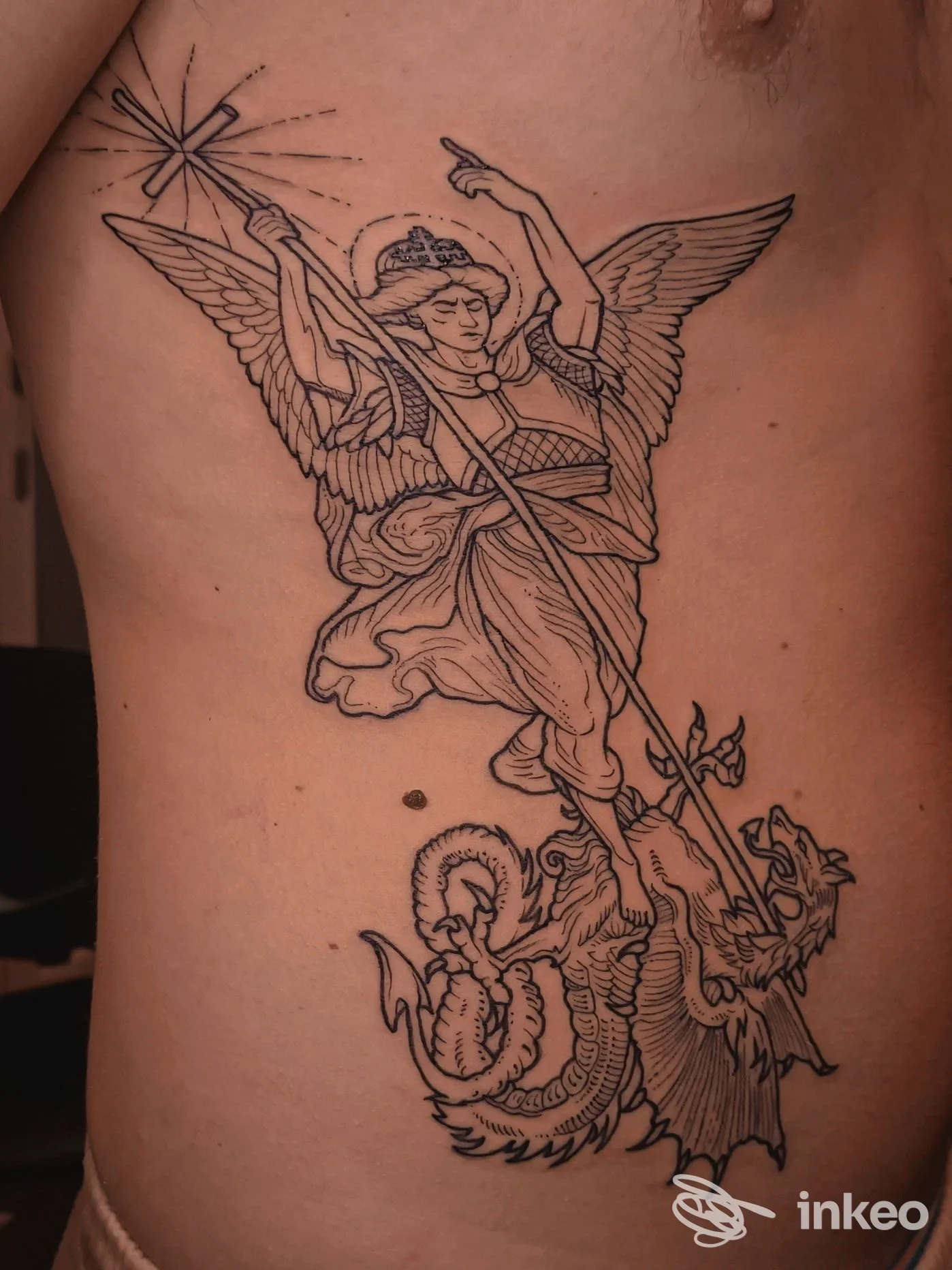 Tatuaggio a linee nere di un angelo che trafigge un drago sul costato, foto inviata da Mystica Body Art Studio, Gattinara.