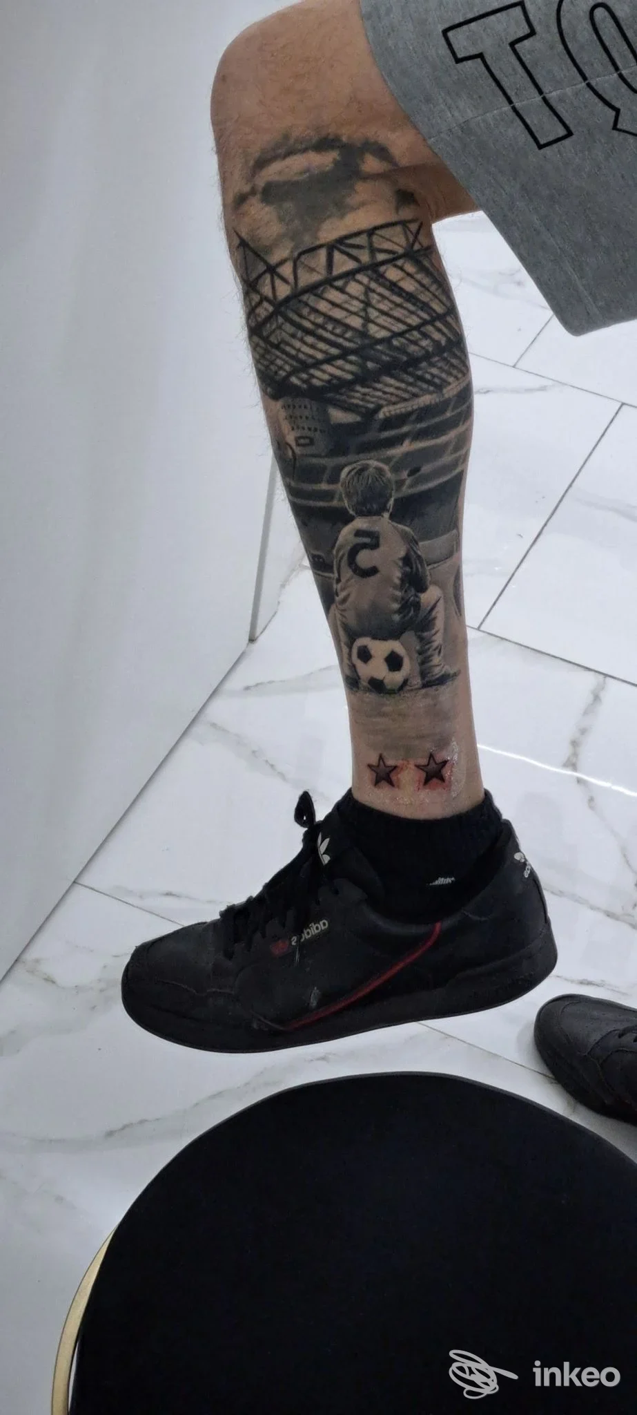 Tattoo su polpaccio visibile: braccio/gamba tatuata con motivo architettonico e figure, scatto in studio COR MEUM Tattoo, Magenta.