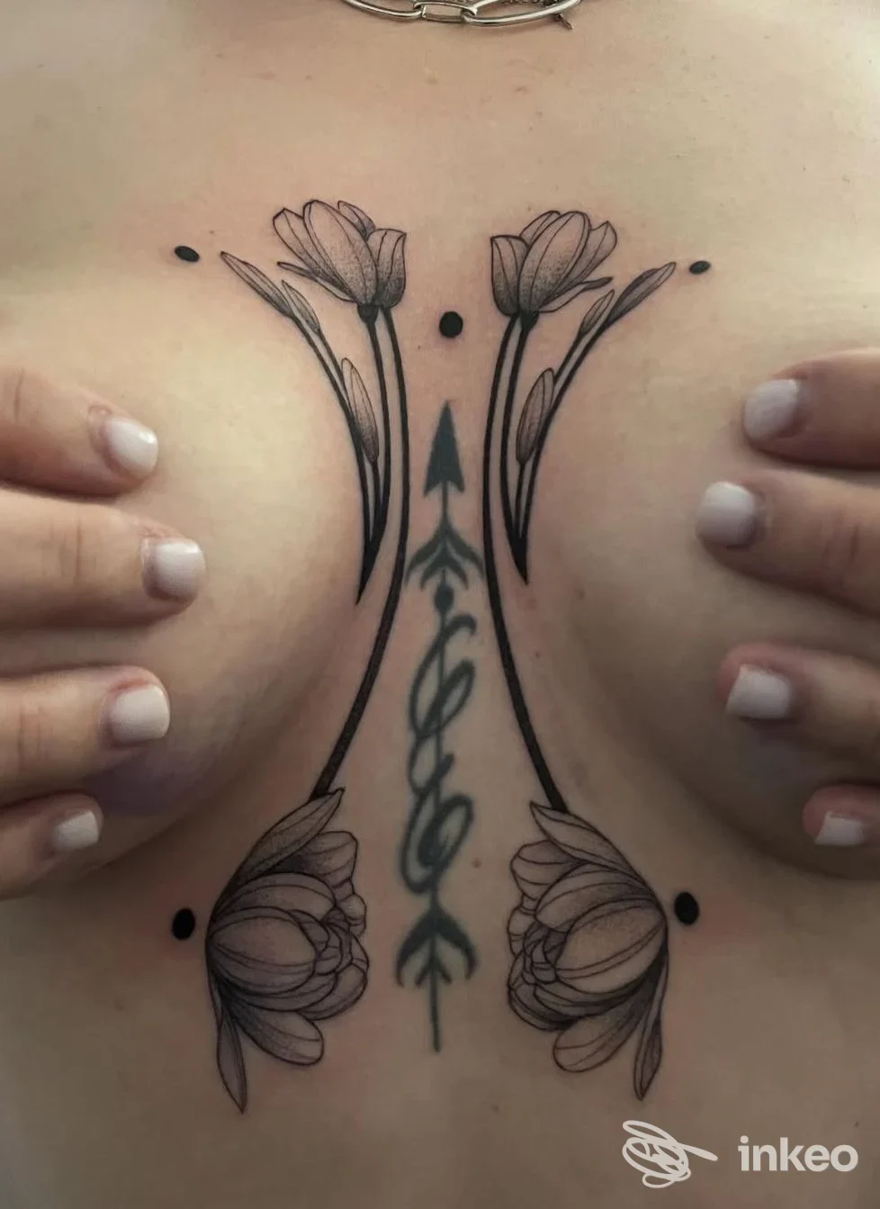 Tattoo inchiostrato nero su pelle della parte alta della schiena, fiori ai lati e motivo centrale a frecce, due mani ai lati sostengono la pelle.
