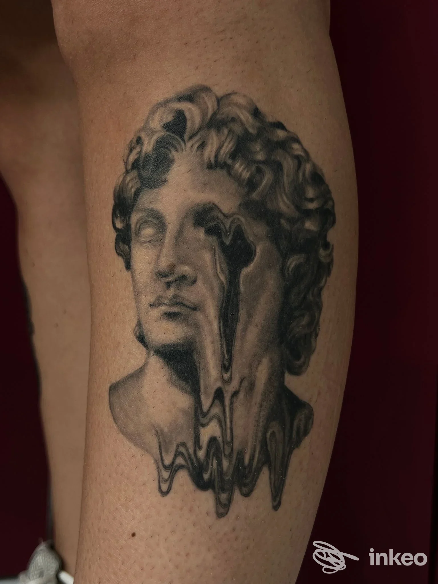 Tatuaggio realistico in bianco e nero di un busto classico che si scioglie sul polpaccio, immagine fornita da Studio Arte Integrata, Cagliari.