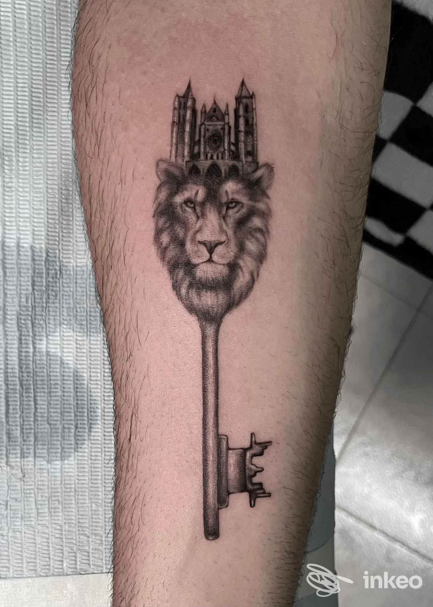 Tatuaggio in bianco e nero sull'avambraccio: testa di leone integrata in una chiave con cattedrale. Studio Arte Integrata, Cagliari.