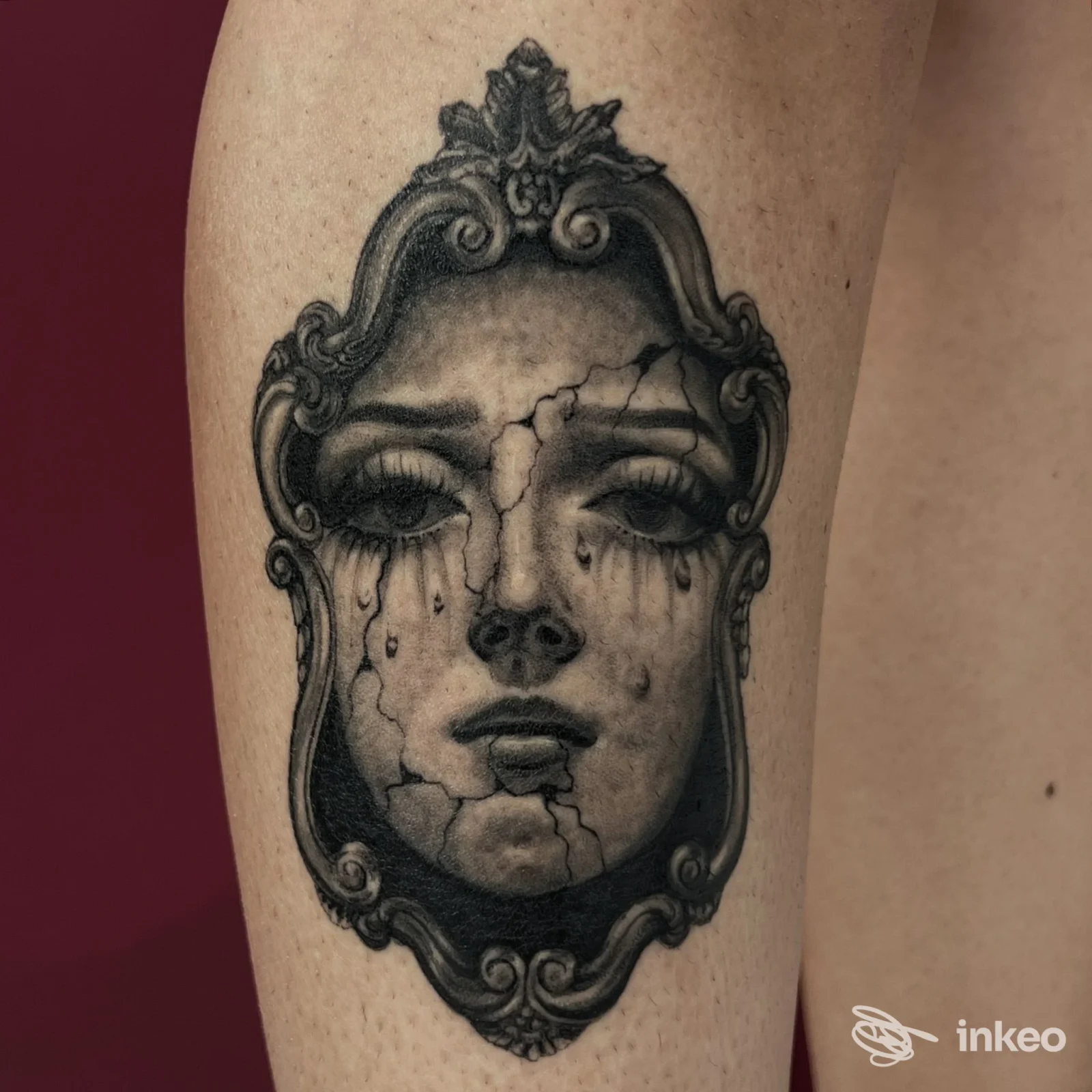 Tatuaggio realistico in bianco e nero di un volto crepato entro cornice, applicato sul polpaccio. Studio Arte Integrata, Cagliari.