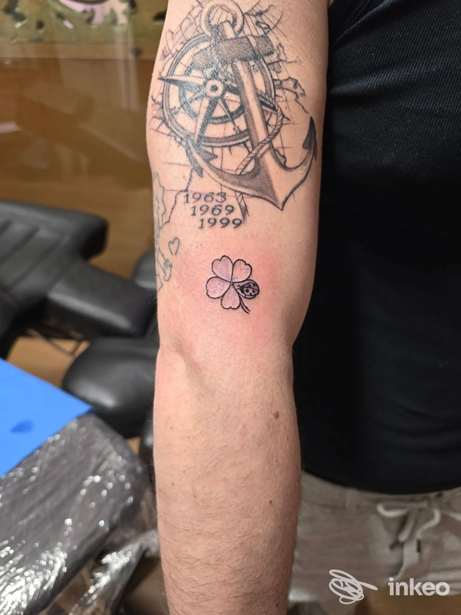 Dettaglio di avambraccio con tatuaggi: timone con ancora e date, e piccolo quadrifoglio con coccinella. Inkme Studio Tattoo & Piercing, Monopoli.