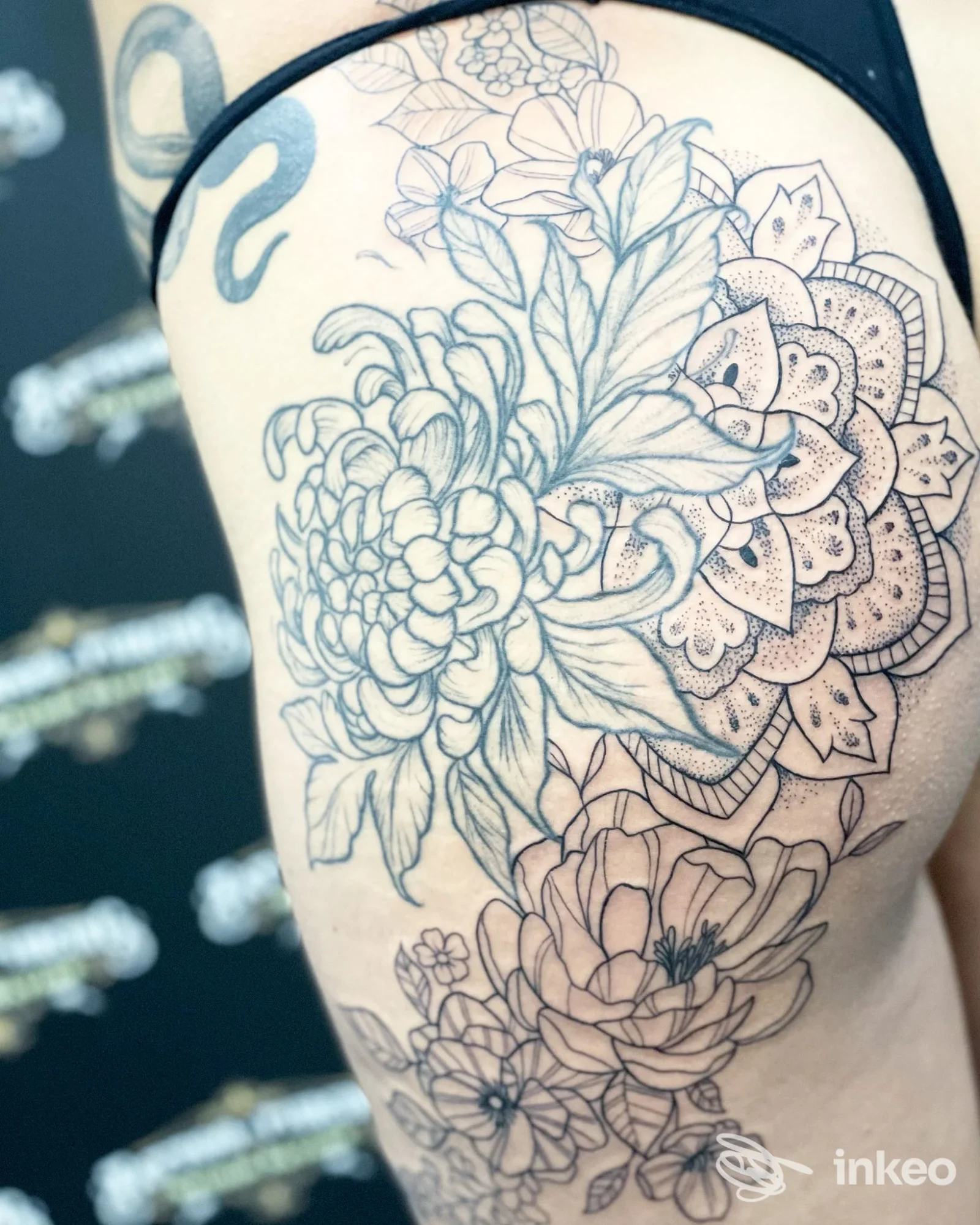 Tattoo floreale su pelle, disegno lineare e dettagli di fiori visibile sulla gamba, con contorni chiari e sfondo sfocato.