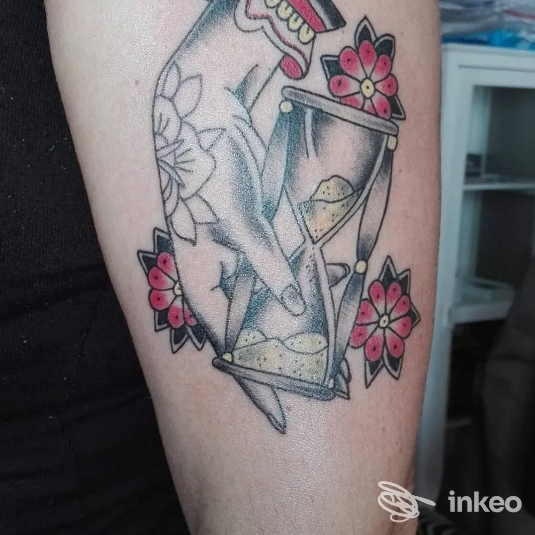 Tatuaggio su avambraccio raffigurante una mano con una clessidra e fiori; foto inviata da Rock 'n' Roll Tattoo Verona, Peschiera del Garda.