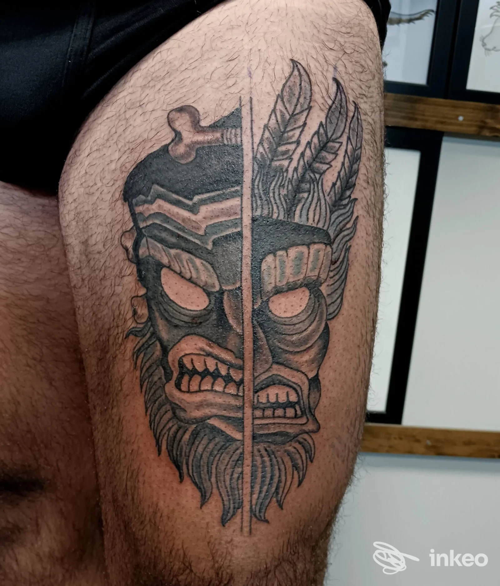 Tatuaggio blackwork su coscia con maschera divisa e piume, foto fornita da Green Valley Tattoo a Verona.