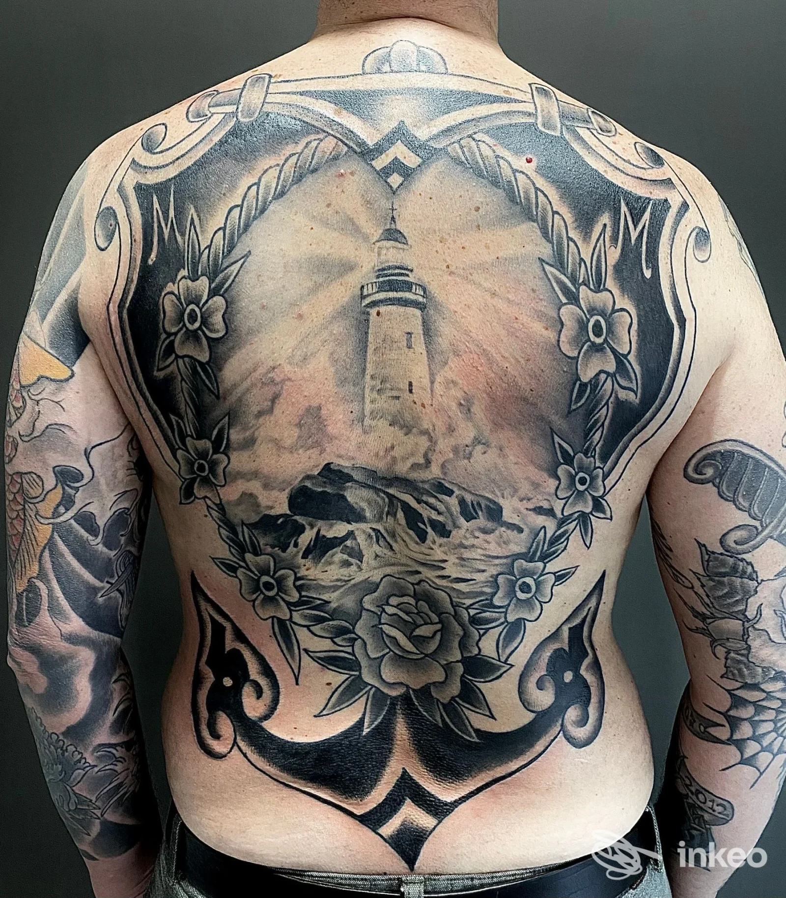 Ampio tatuaggio schiena con faro, onde e decorazioni floreali — CAONTATTOO STUDIO, Viterbo.
