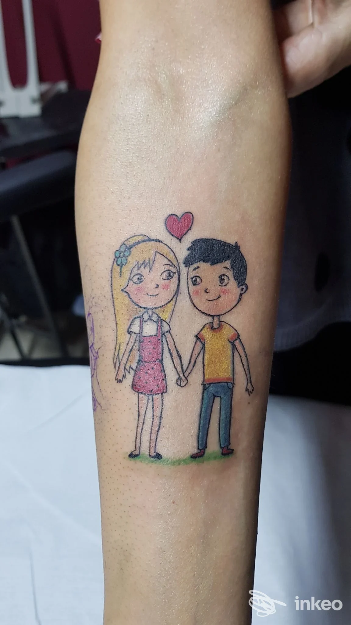 Tatuaggio sull'avambraccio con due personaggi stilizzati che si tengono per mano, Tora Tattoo, Rio Saliceto.