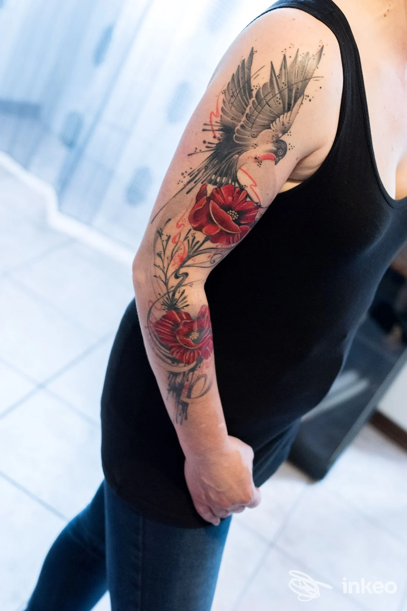 Braccio tatuato con colomba e fiori rossi, fotografia per Tattoo Rudy a Meina.