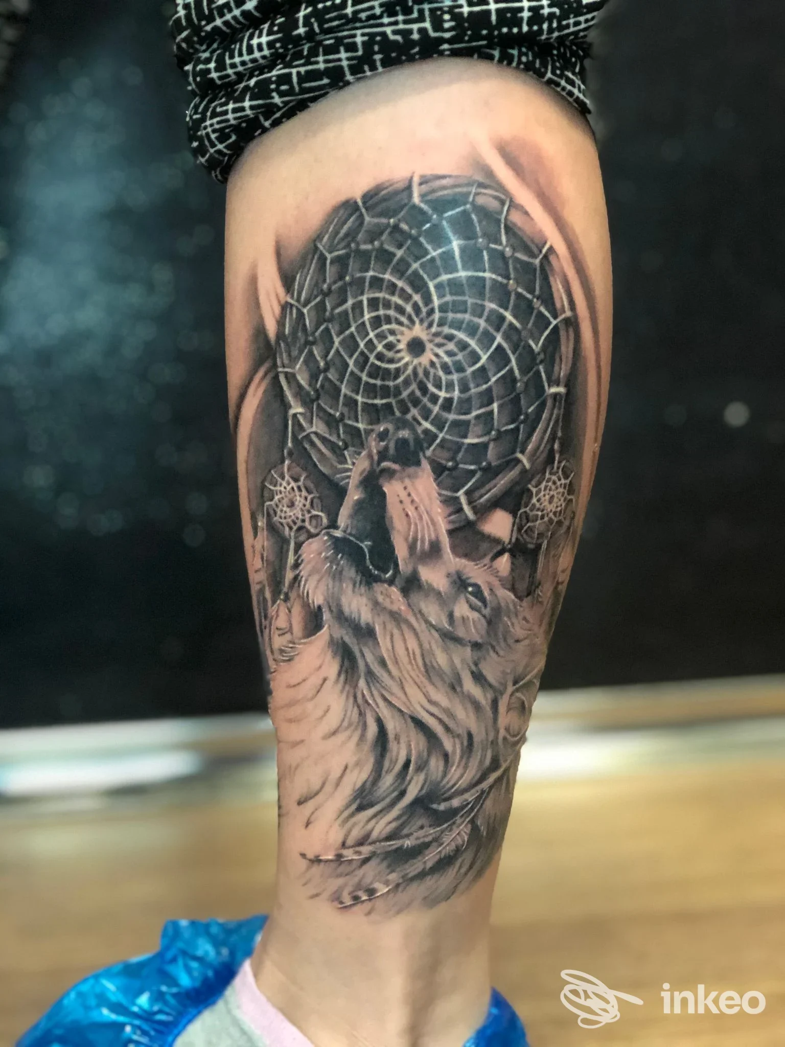 Tatuaggio realistico su polpaccio con lupo che ulula e acchiappasogni, foto da Indaco Tattoo crew a Torino.