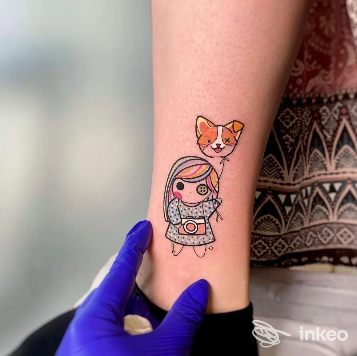 Tatuaggio colorato di bambolina e palloncino-gatto sulla caviglia, fotografato nello studio Avant-Garde Ink Tattoo & Piercing a Sona.