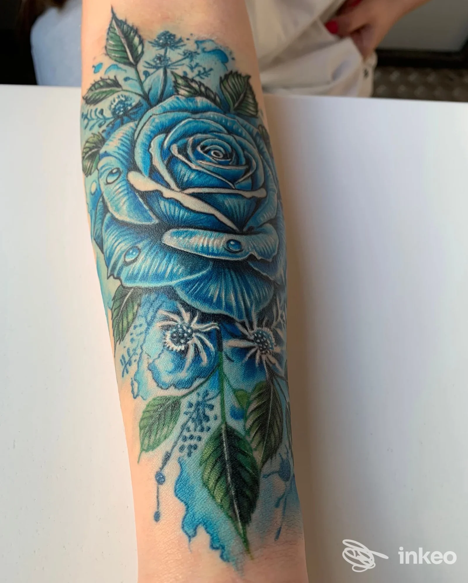 Tatuaggio a rosa blu sull'avambraccio realizzato da DINO TATTOO a Molfetta, dettaglio floreale e foglie in verde e blu.