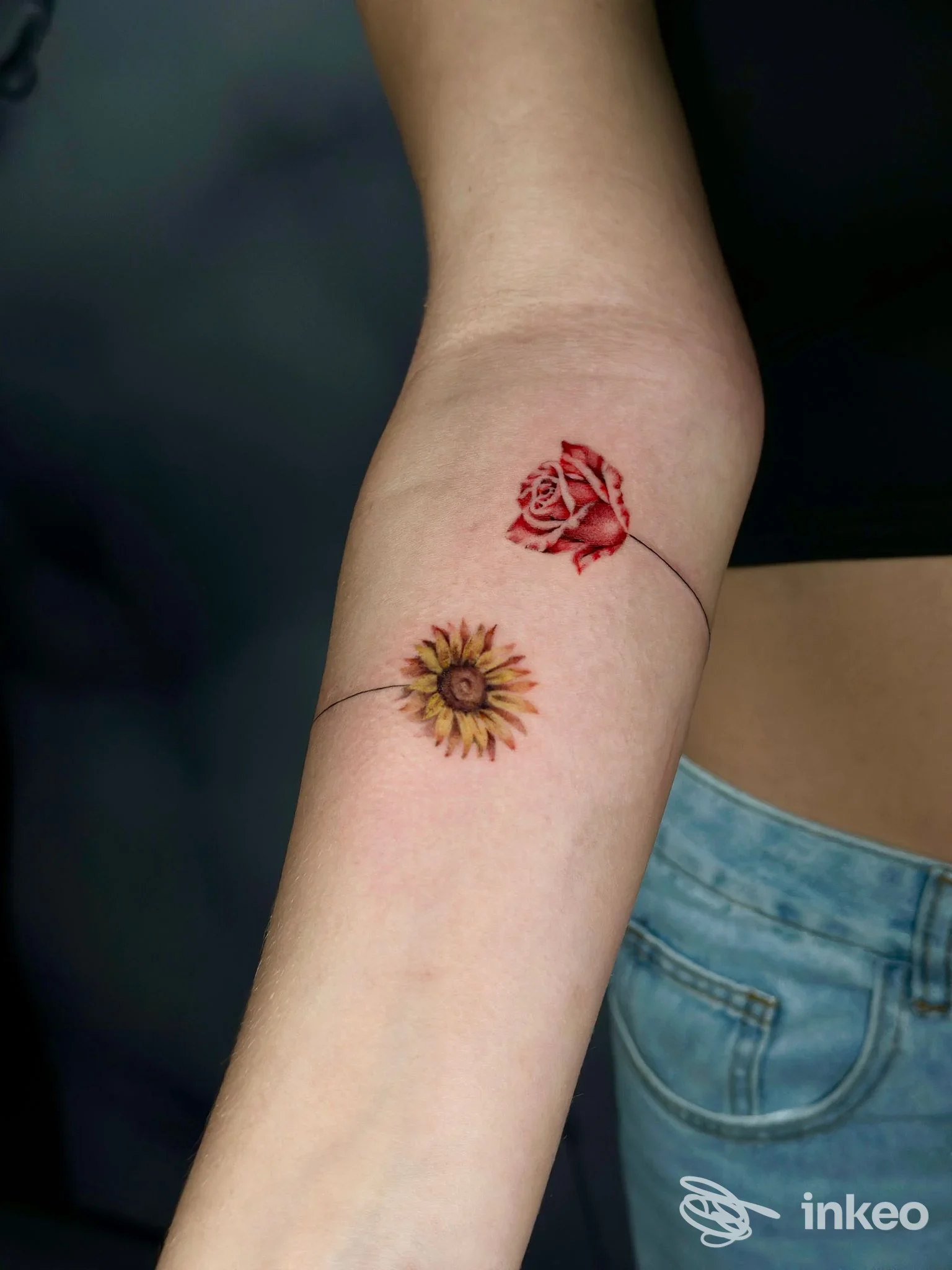 Doppio tatuaggio floreale sull'avambraccio: una rosa rossa e un girasole collegati da un sottile filo. Twenty Ink Studio, Barletta.