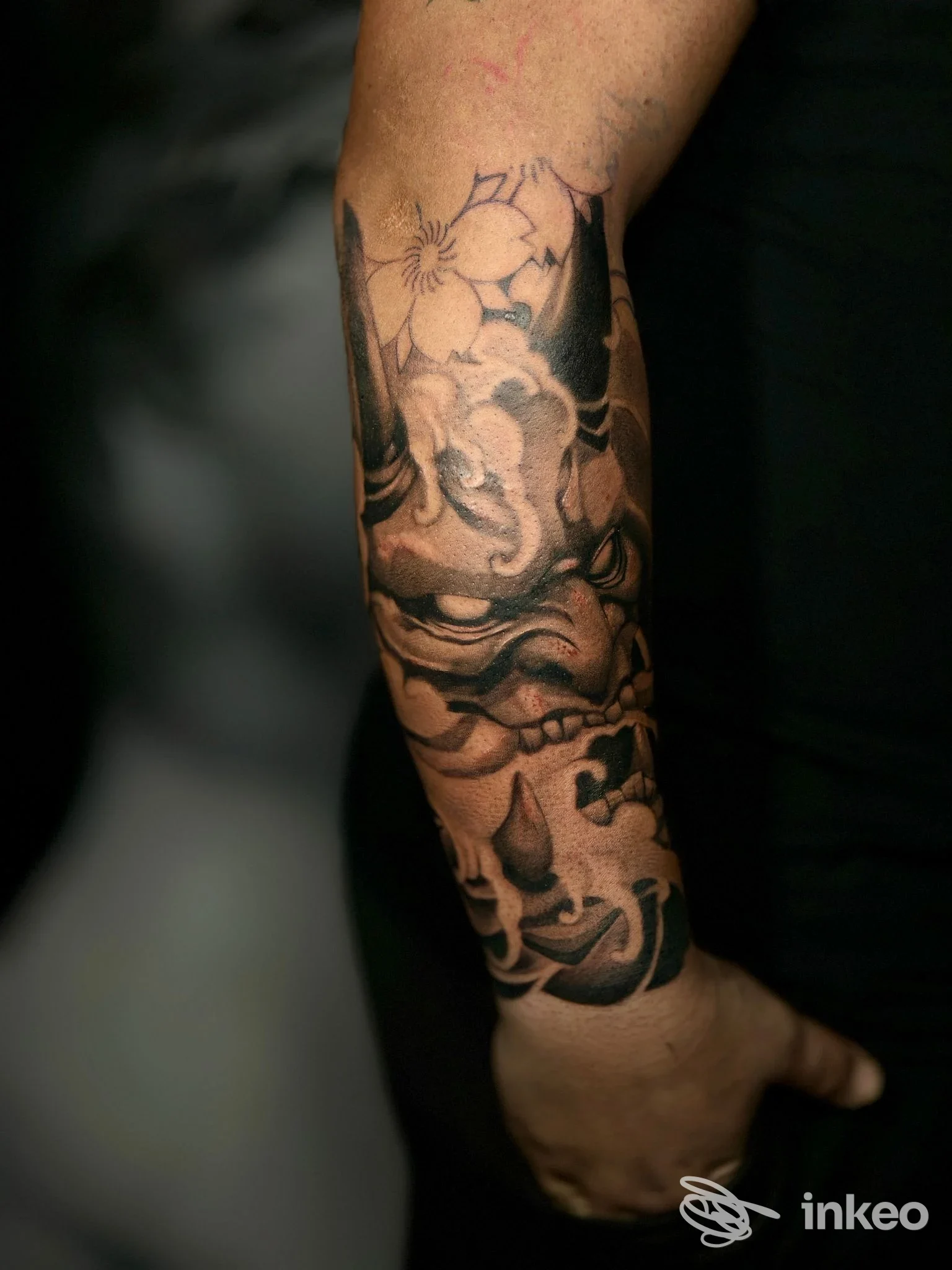 Tatuaggio black & grey su avambraccio realizzato da Twenty Ink Studio a Barletta, maschera stilizzata e fiori.