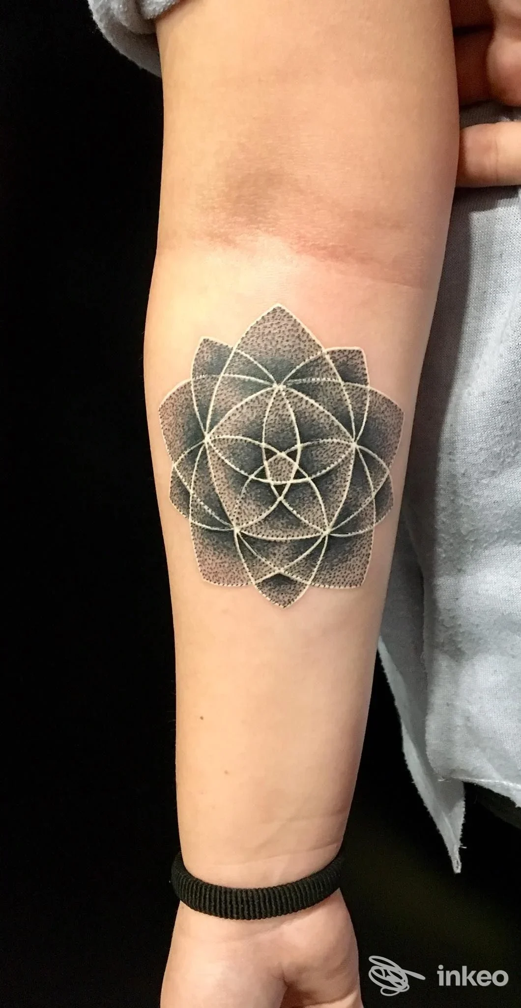 Tattoo geometrico a mandala su avambraccio, afro di colori neri. Primo piano su braccio sinistro, senza volto visibile, in studio.