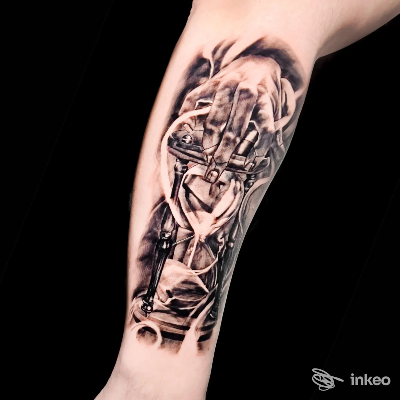 Tatuaggio realistico in bianco e nero sull'avambraccio: una mano meccanica o componenti ingranaggi sfumati, senza testo né elementi extra.