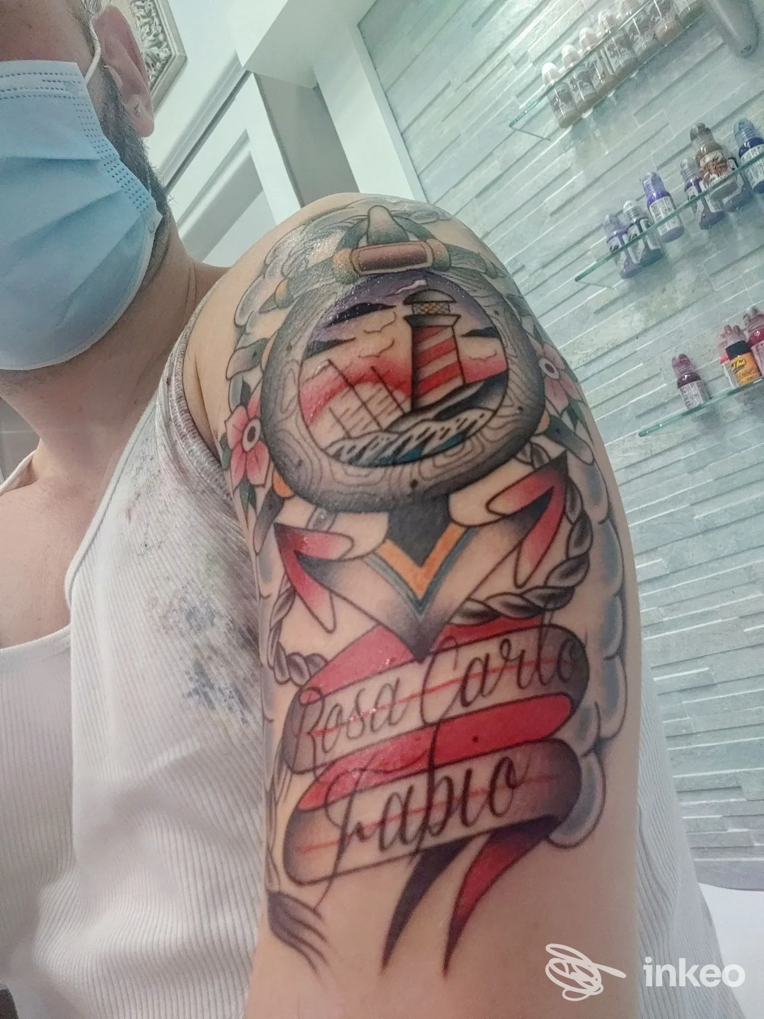 Tatuaggio a colori sulla spalla con faro e nastro, foto dallo studio Alter Ego a Genova.