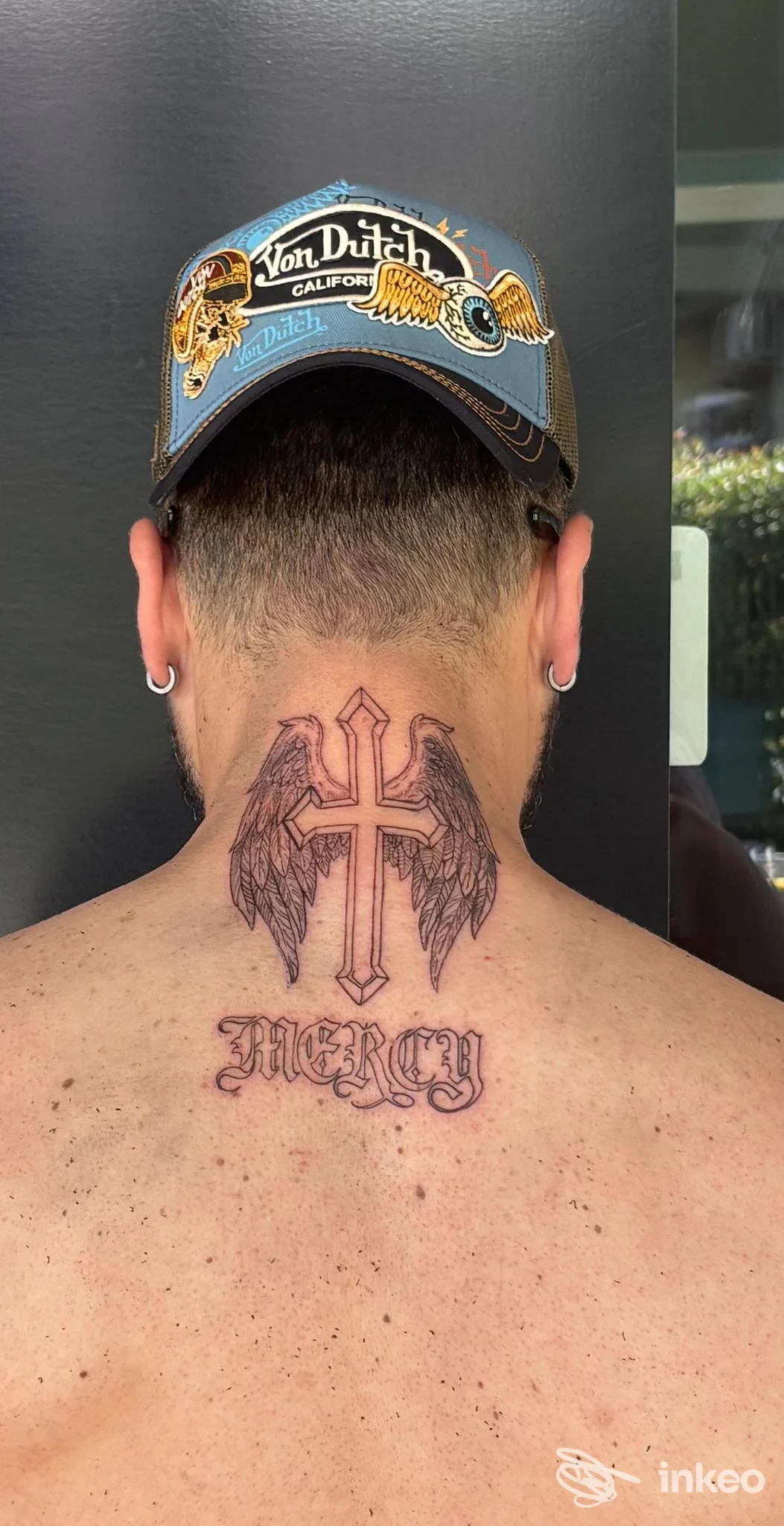 Tatuaggio sul collo con croce alata e scritta 'MERCY', visto dalla nuca. Studio La Bruma, San Lorenzo al Mare.