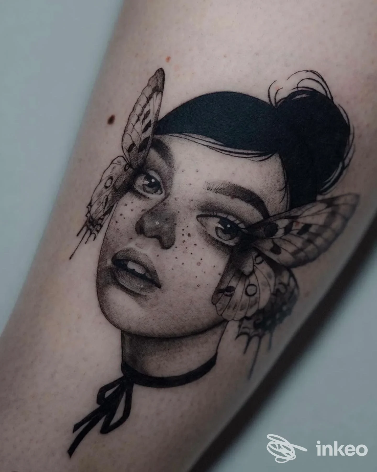Tatuaggio realistico in bianco e nero di volto femminile con falene sull'avambraccio, Lost Love Tattoo Studio, Monterotondo.