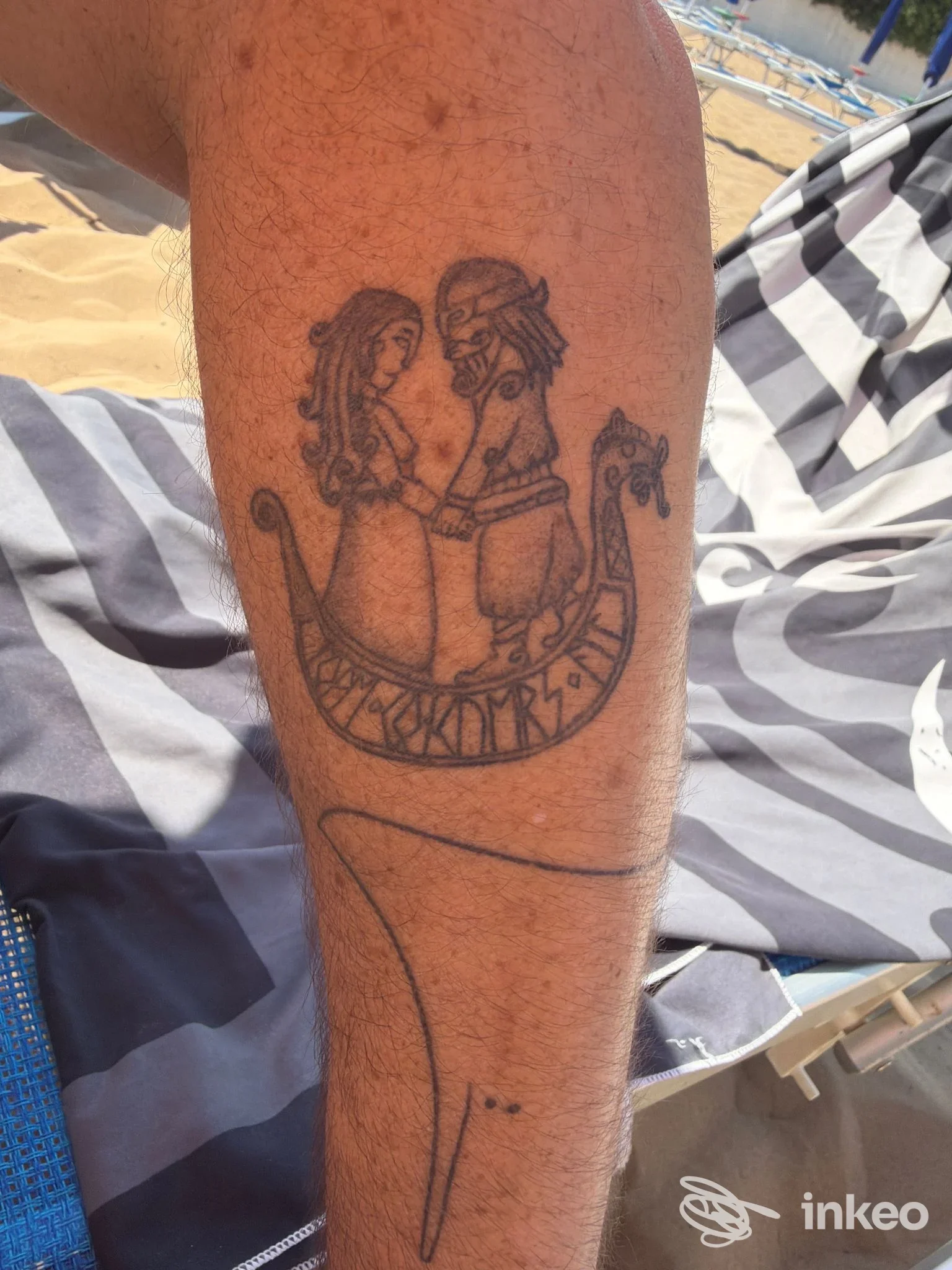 Tatuaggio nero su polpaccio/avambraccio raffigurante due figure in una piccola imbarcazione; immagine fornita da Noire Atelier, Bolzano.