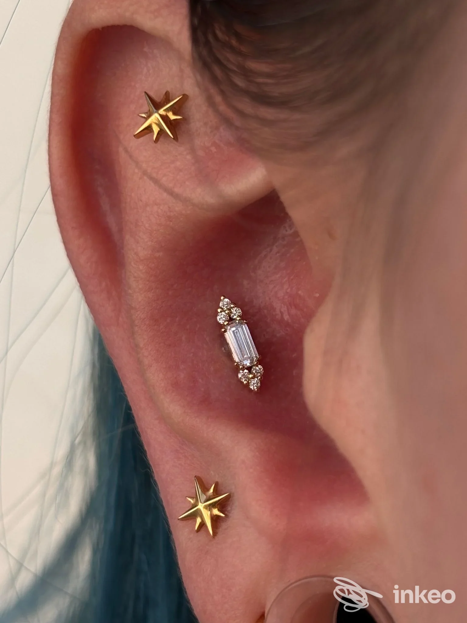 Primo piano di un orecchio con tre piercing dorati nella conca e nel lobo, foto per Cinnie Bodypiercer a Trieste.