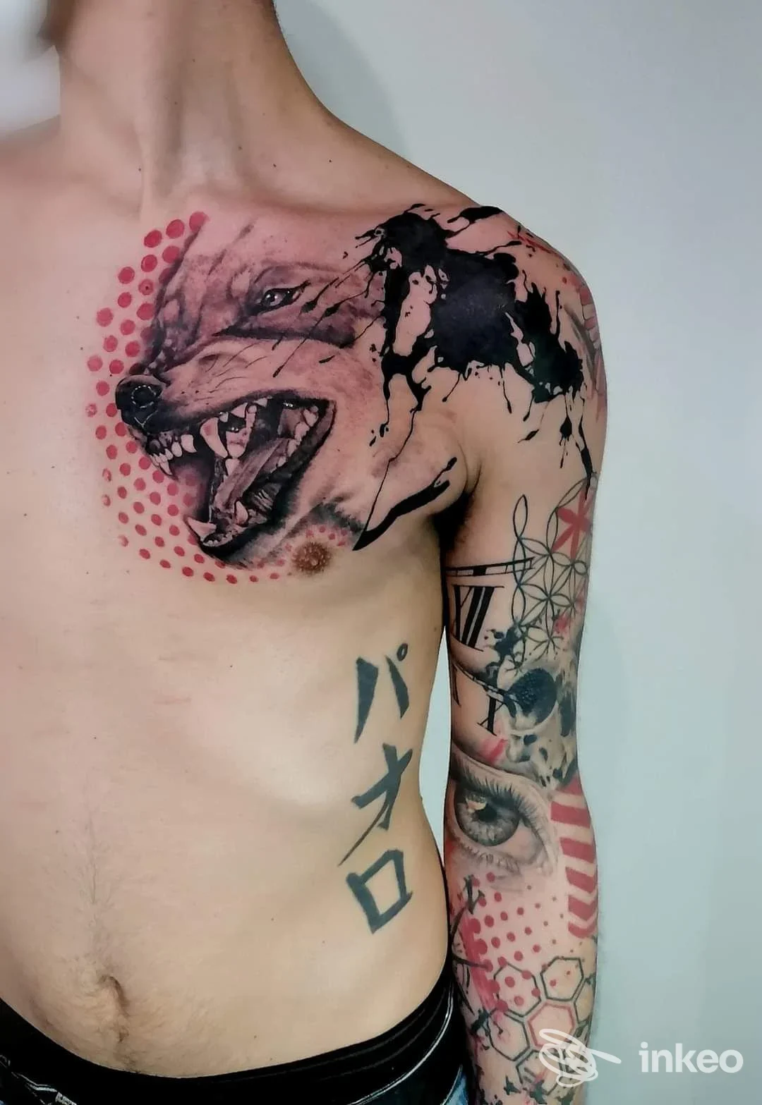 Tattoo realistico di lupo sul torace sinistro con ulteriori tatuaggi sul braccio sinistro, inclusi motivi geometrici, figure e puntinato rosso; nessun volto intero visibile.