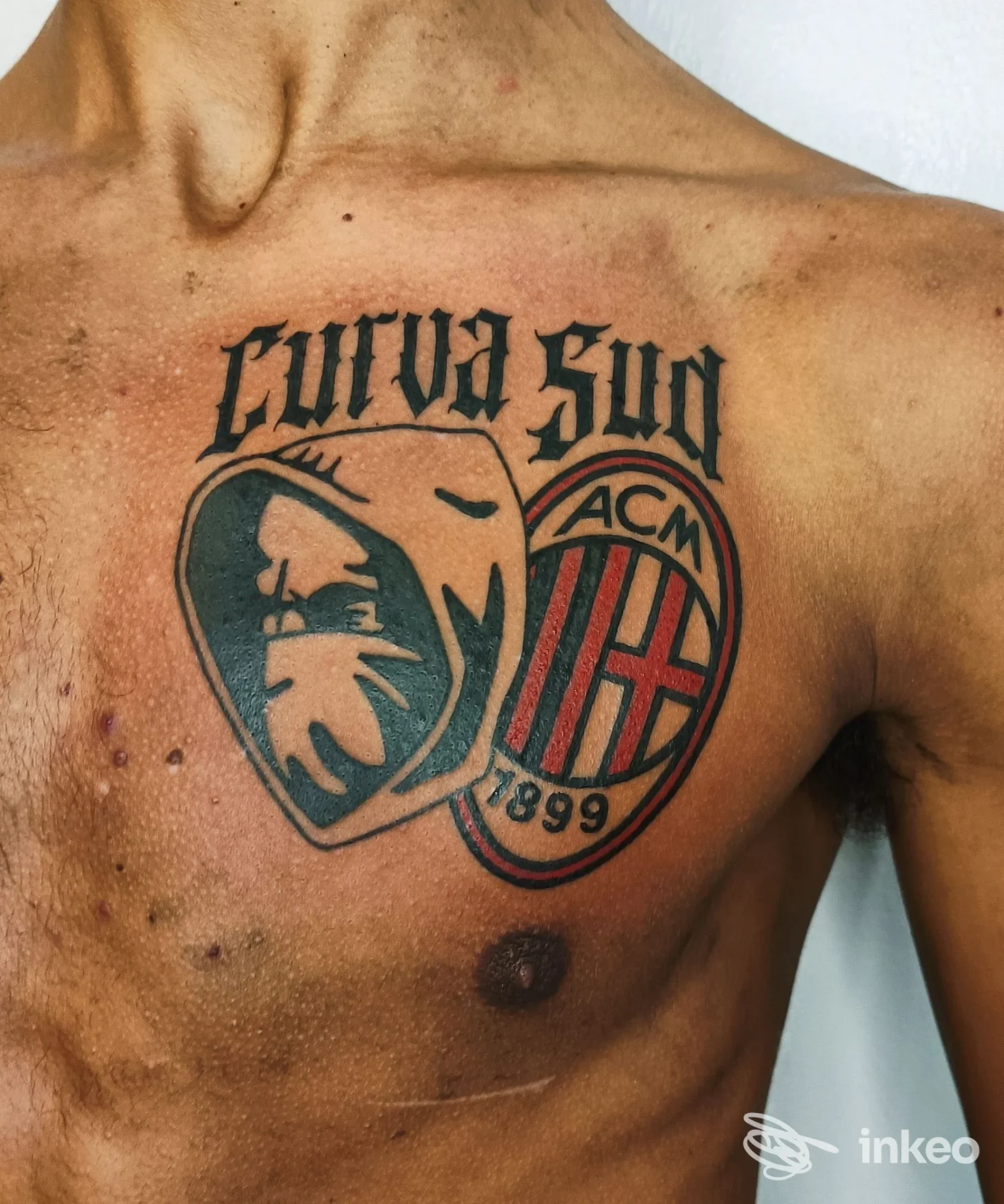 Tattoo sul petto sinistro: grande grafica con stemmi e testo, rifinita in colori scuri su pelle reale, foto singola senza overlay.