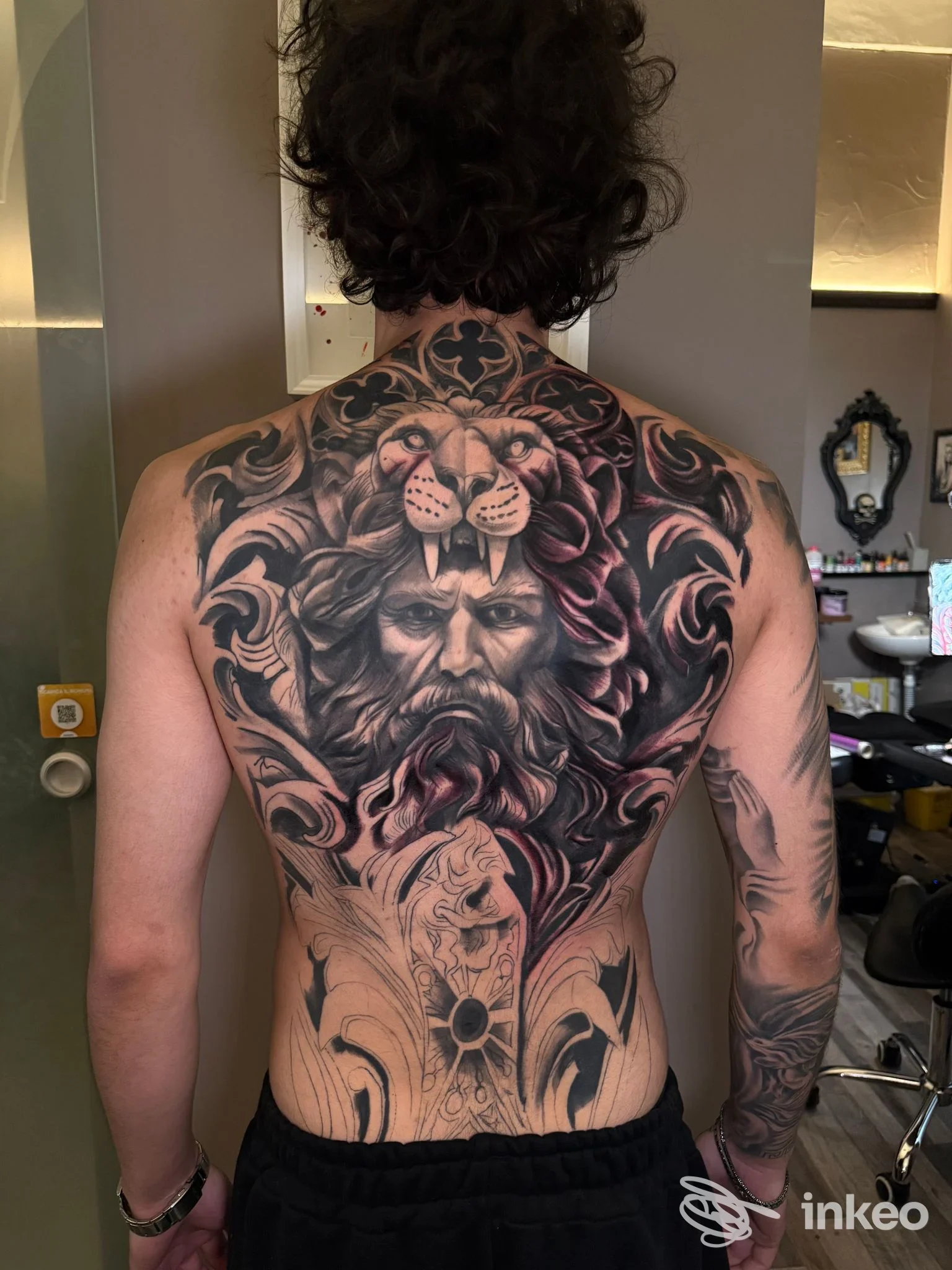 Grande tatuaggio black & grey sulla schiena realizzato da Ro barber tattoo, Lecce, raffigurante un leone e un volto barbuto ornamentale.